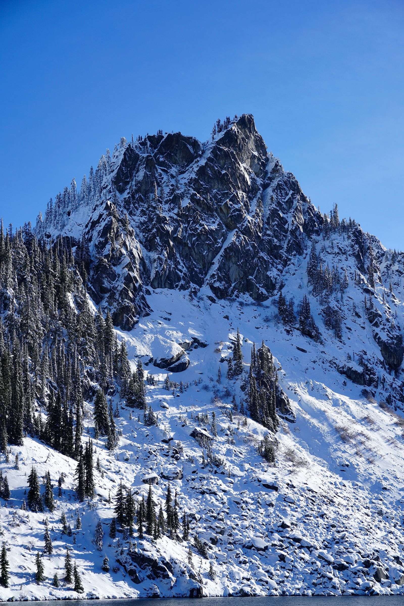 Snow-covered rocky peak above snowy slopes with exposed boulders, Lake Valhalla