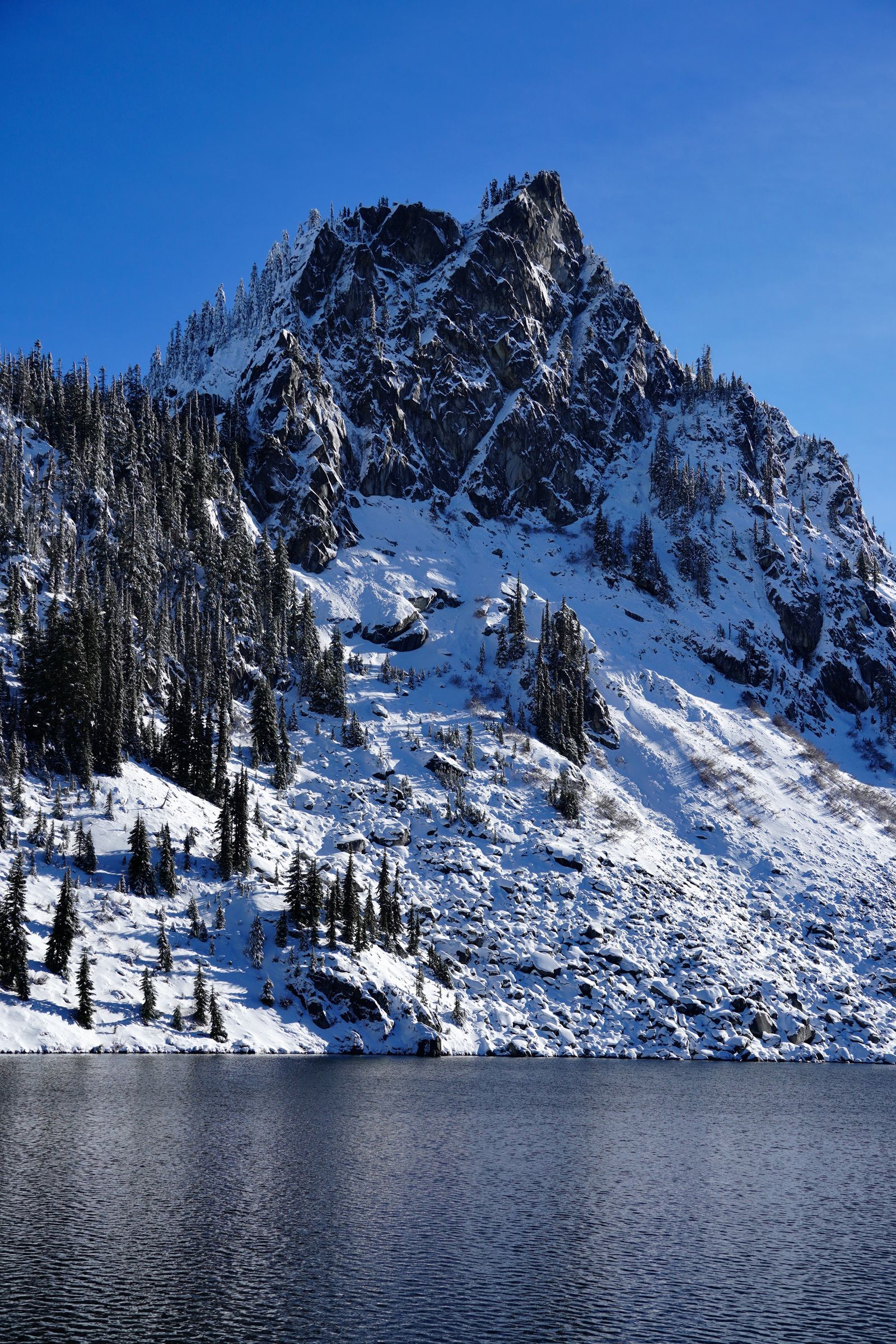 Snow-covered rocky peak above rippling Lake Valhalla