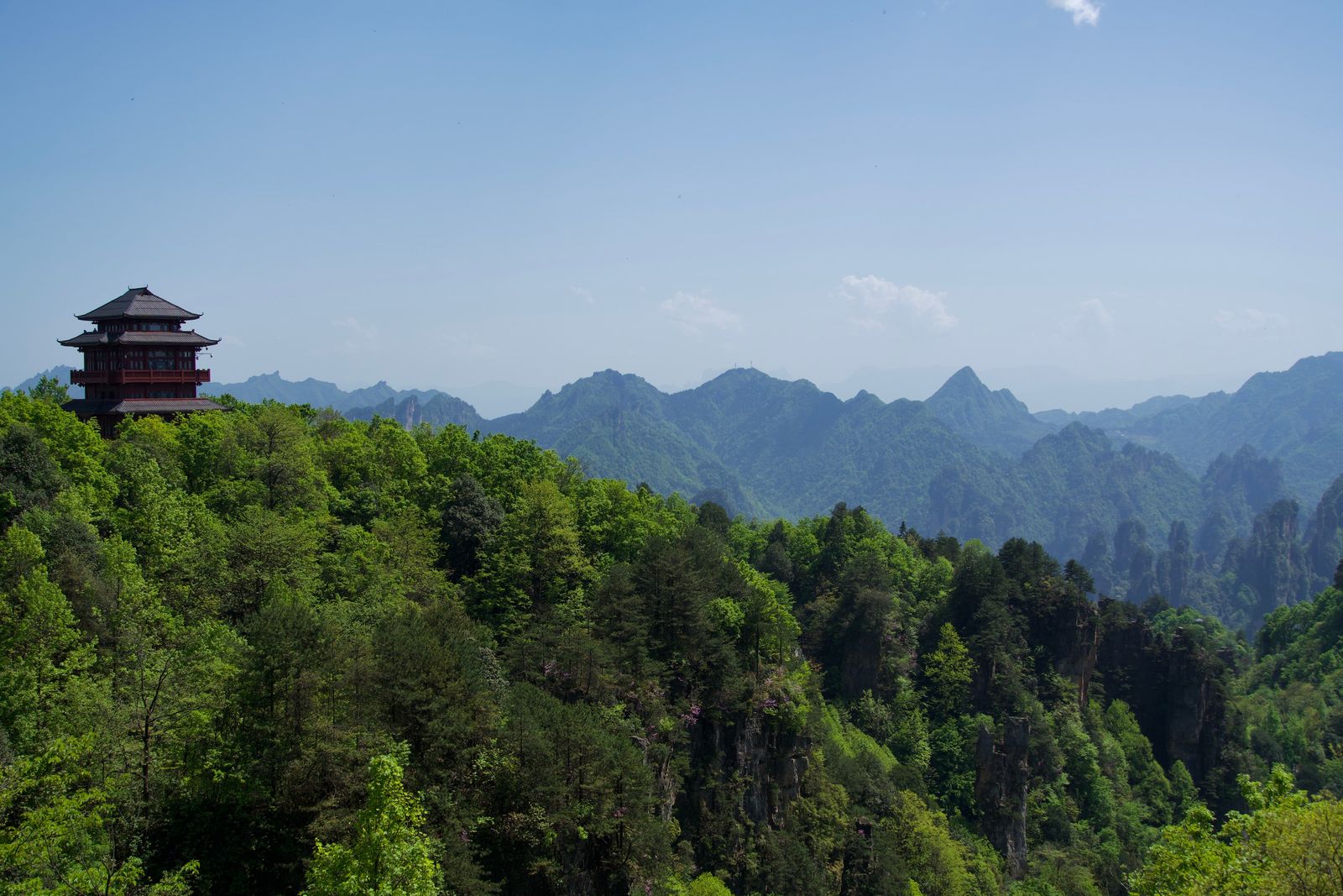 Forested peaks beyond a ridge with a tiered red building, Zhangjiajie