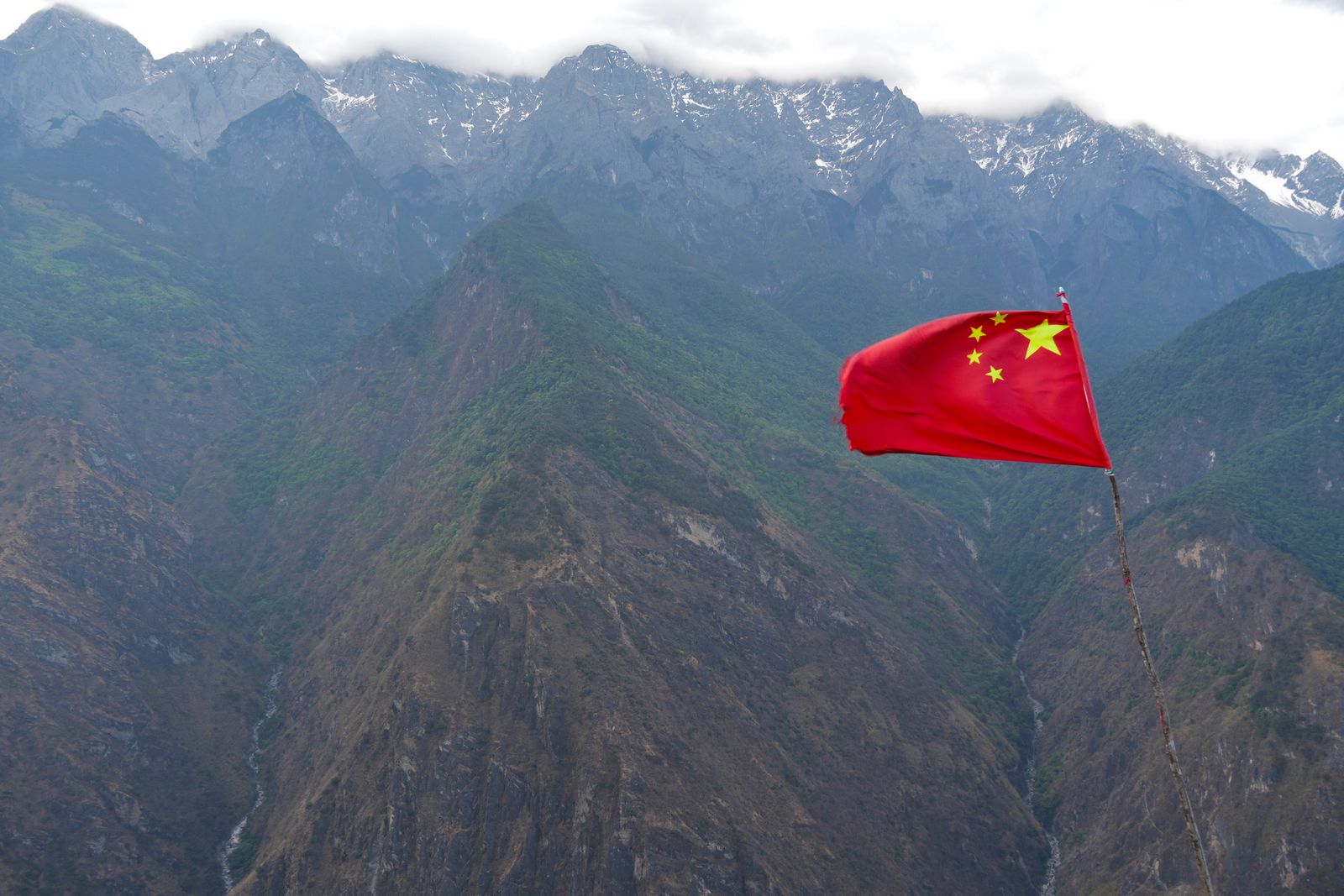 Red flag with yellow stars below snow-streaked mountains, Tiger Leaping Gorge