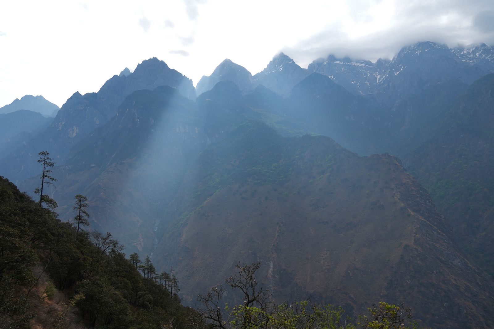 Mountain peaks above a wooded trail in shafts of sunlight, Tiger Leaping Gorge
