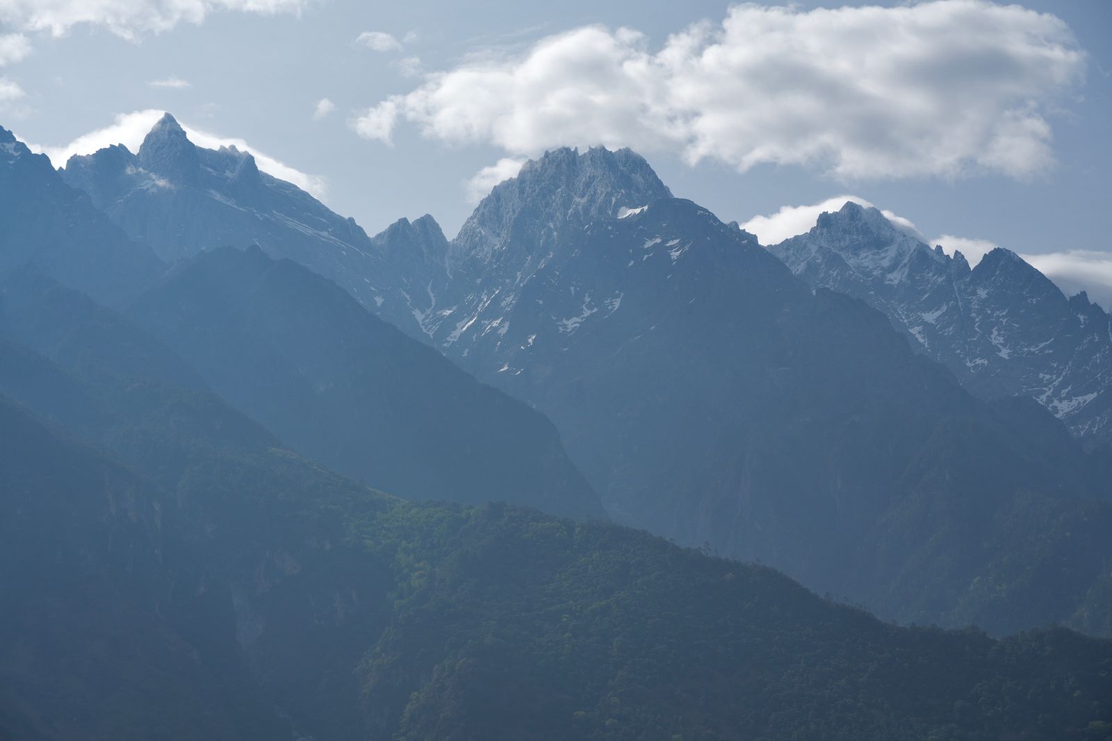Snow-patched mountain peaks above wooded slopes in haze, Tiger Leaping Gorge