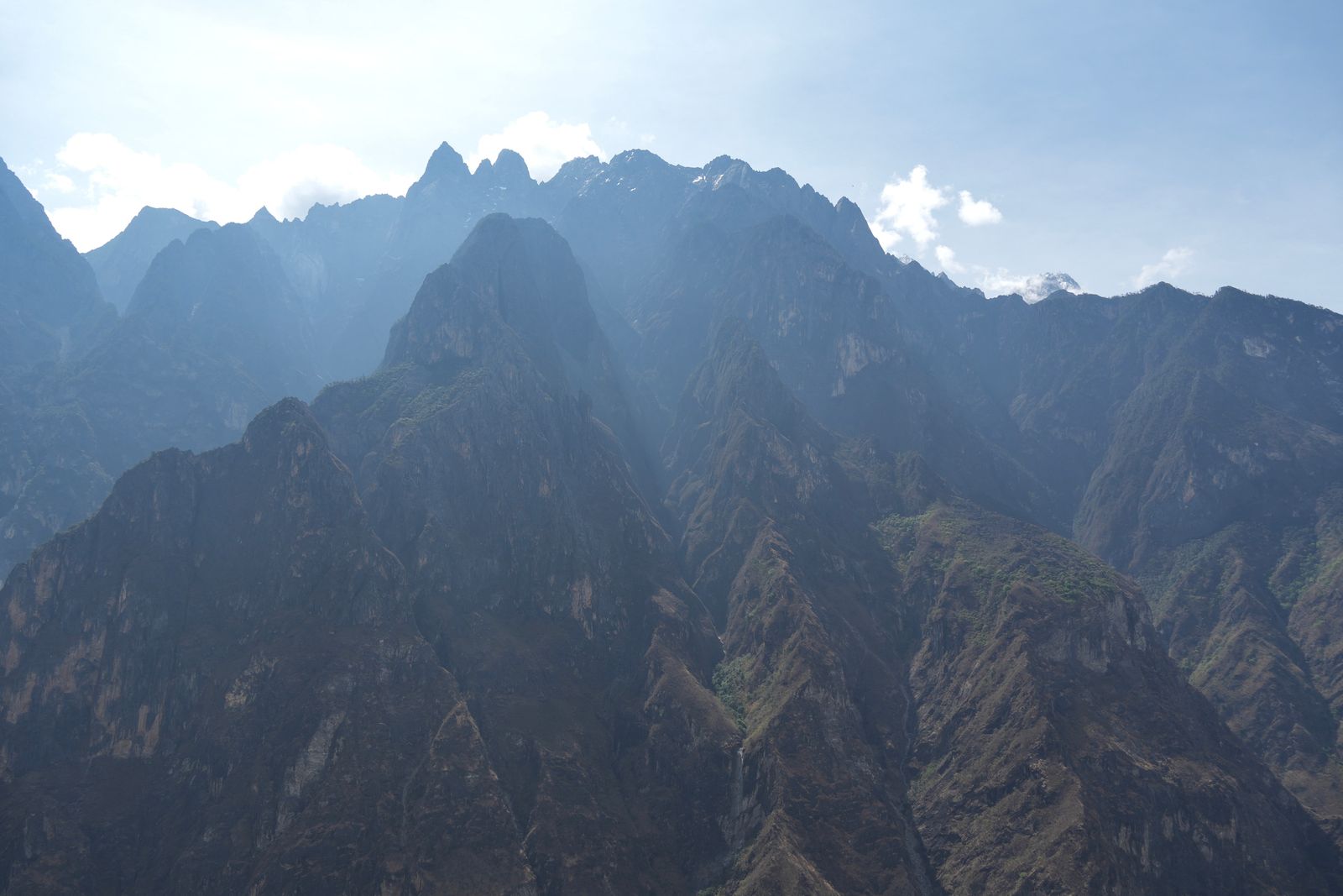 Backlit mountain ridges above rocky slopes with patches of greenery, Tiger Leaping Gorge