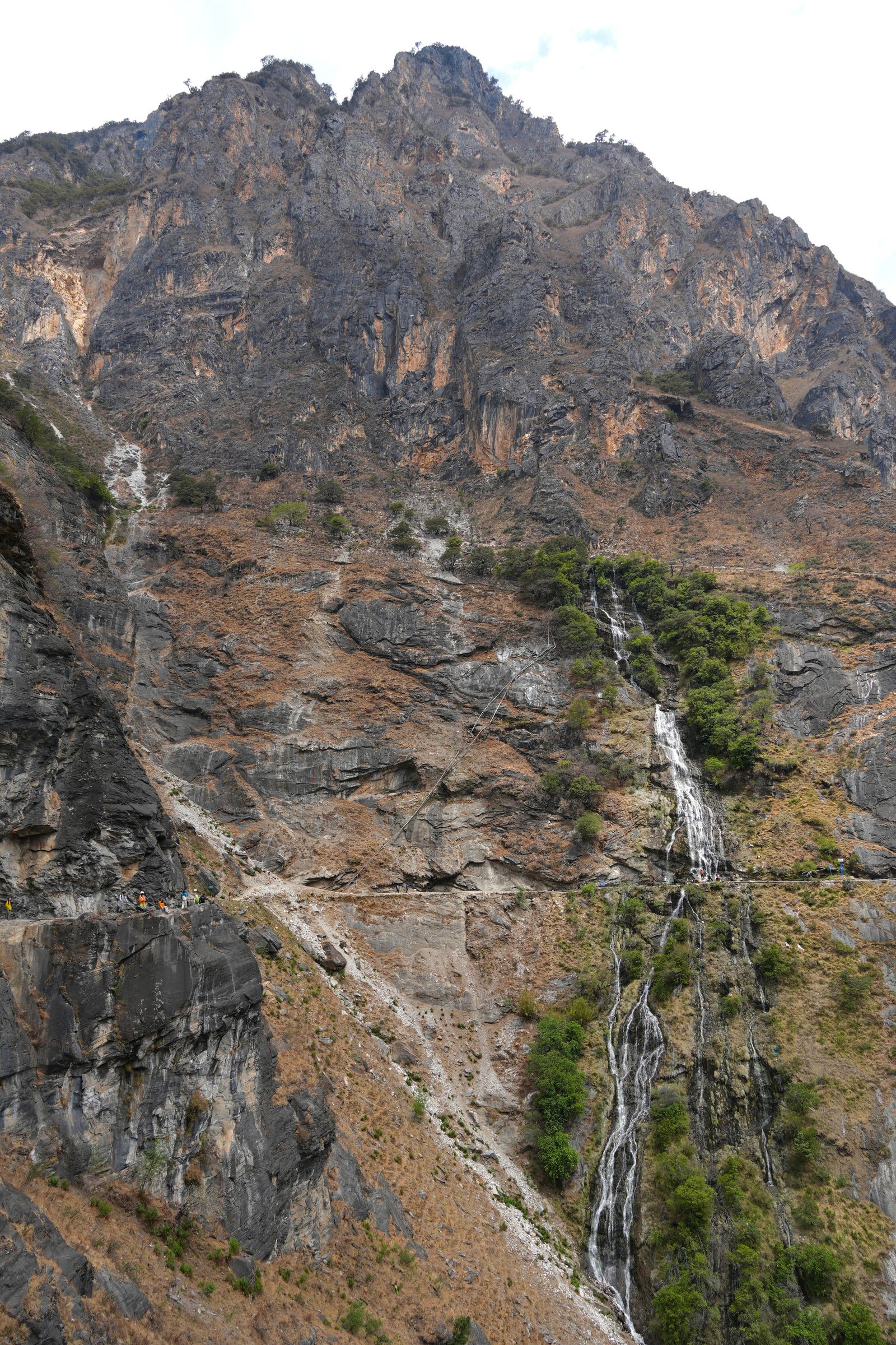 Waterfall cascading down a rocky cliff crossed by hikers, Tiger Leaping Gorge