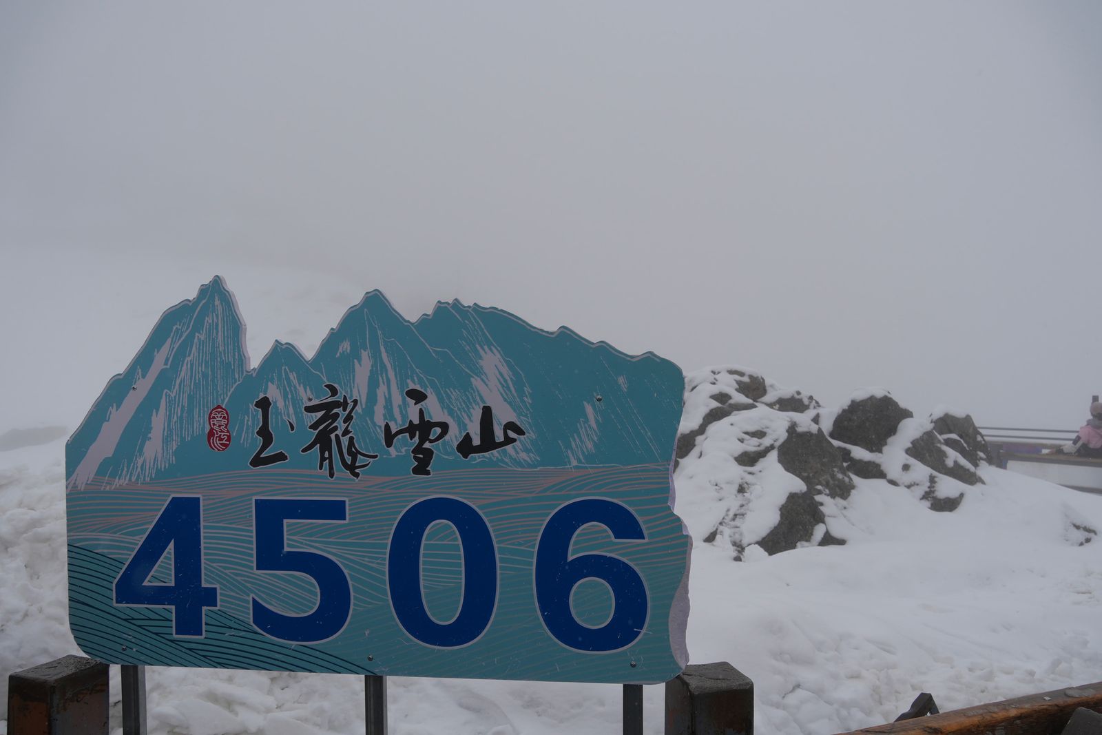 A turquoise 4506 sign beside snow-covered rocks in fog, Tiger Leaping Gorge