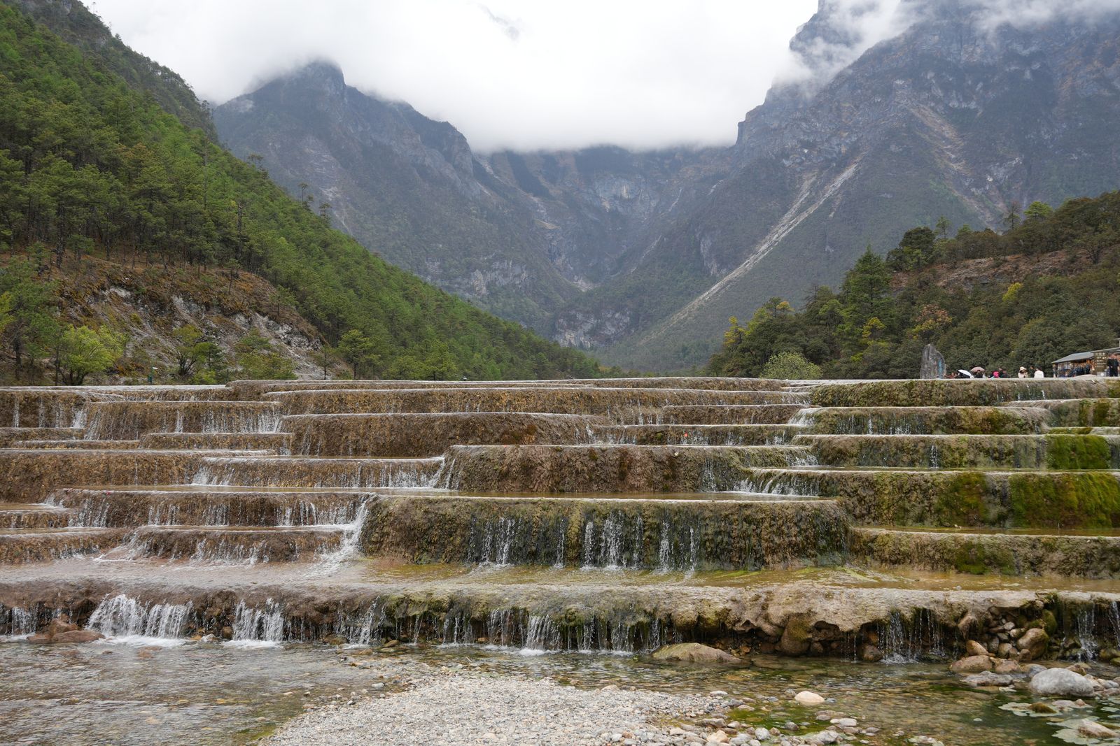 Terraced waterfall below forested mountains in low cloud, Tiger Leaping Gorge
