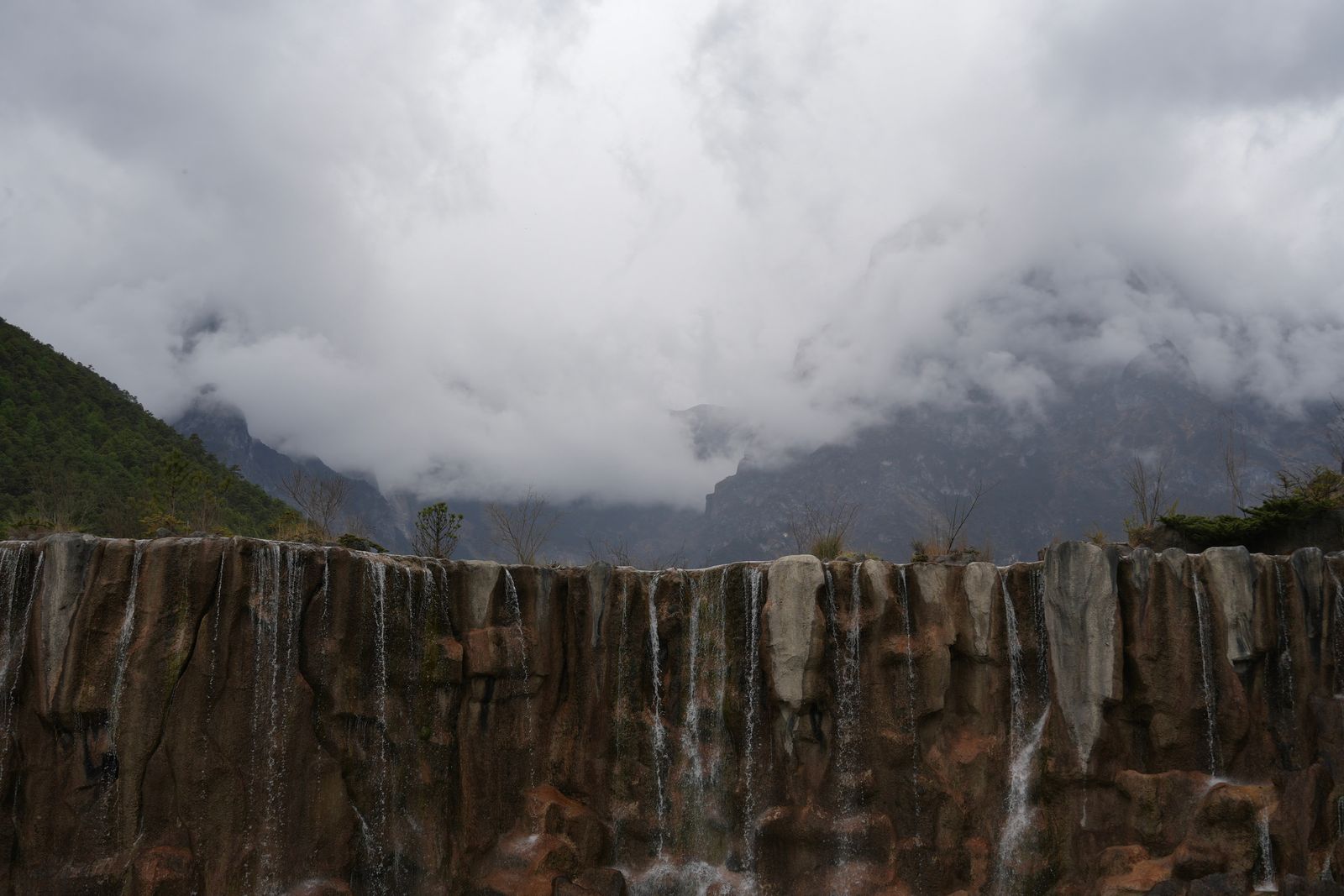 Waterfall cascading down a rock face below cloud-covered mountains, Tiger Leaping Gorge