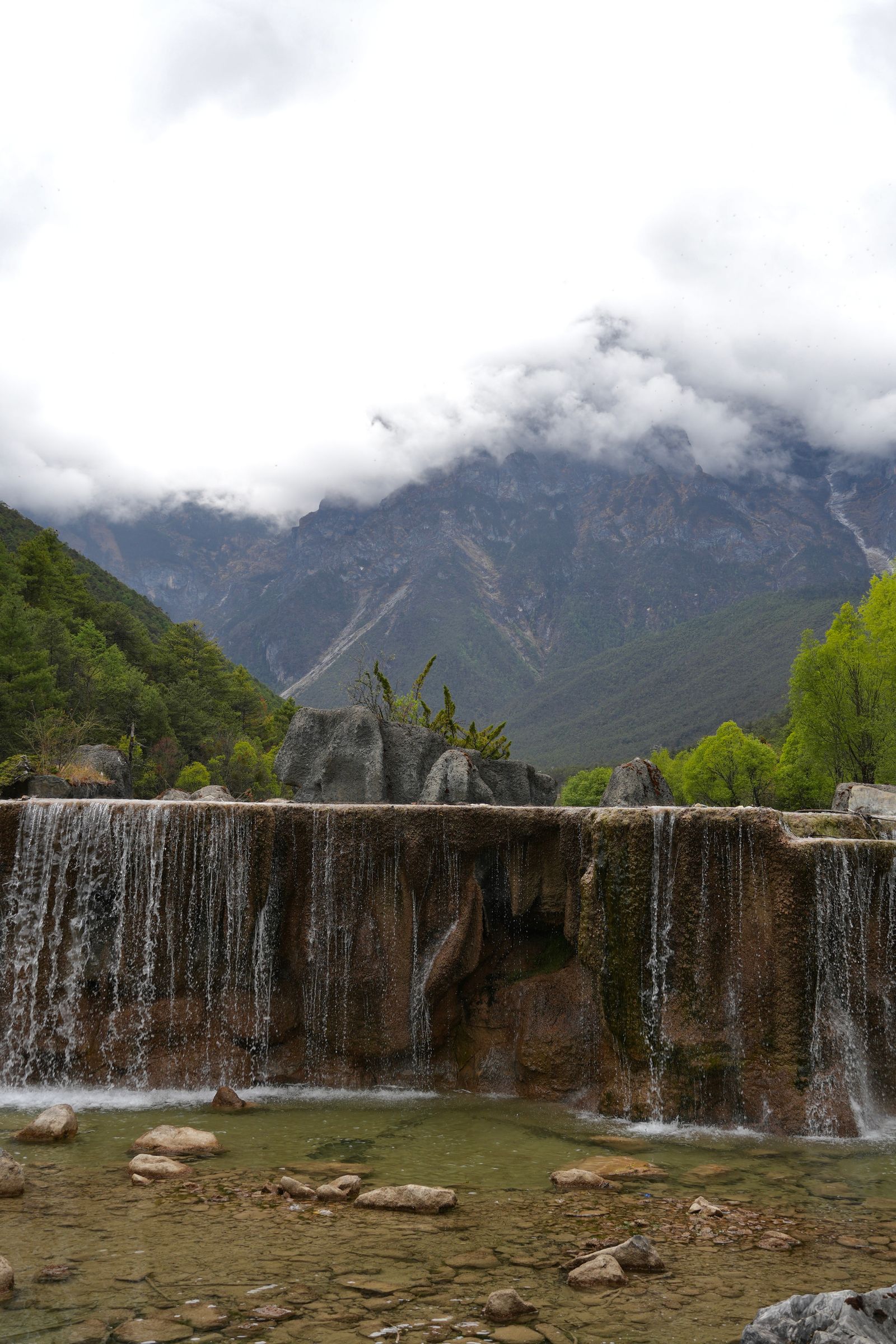 Waterfall over a broad ledge below cloud-covered mountains, Tiger Leaping Gorge
