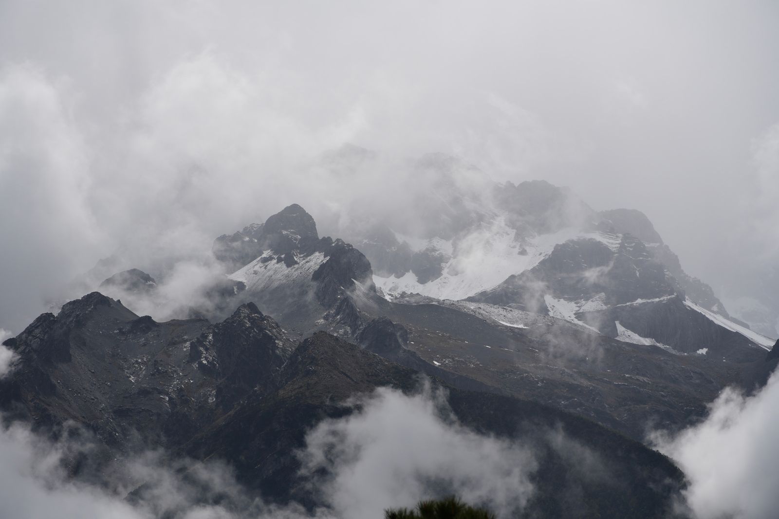 Snow-covered peaks above rocky ridges and forest in low cloud, Tiger Leaping Gorge