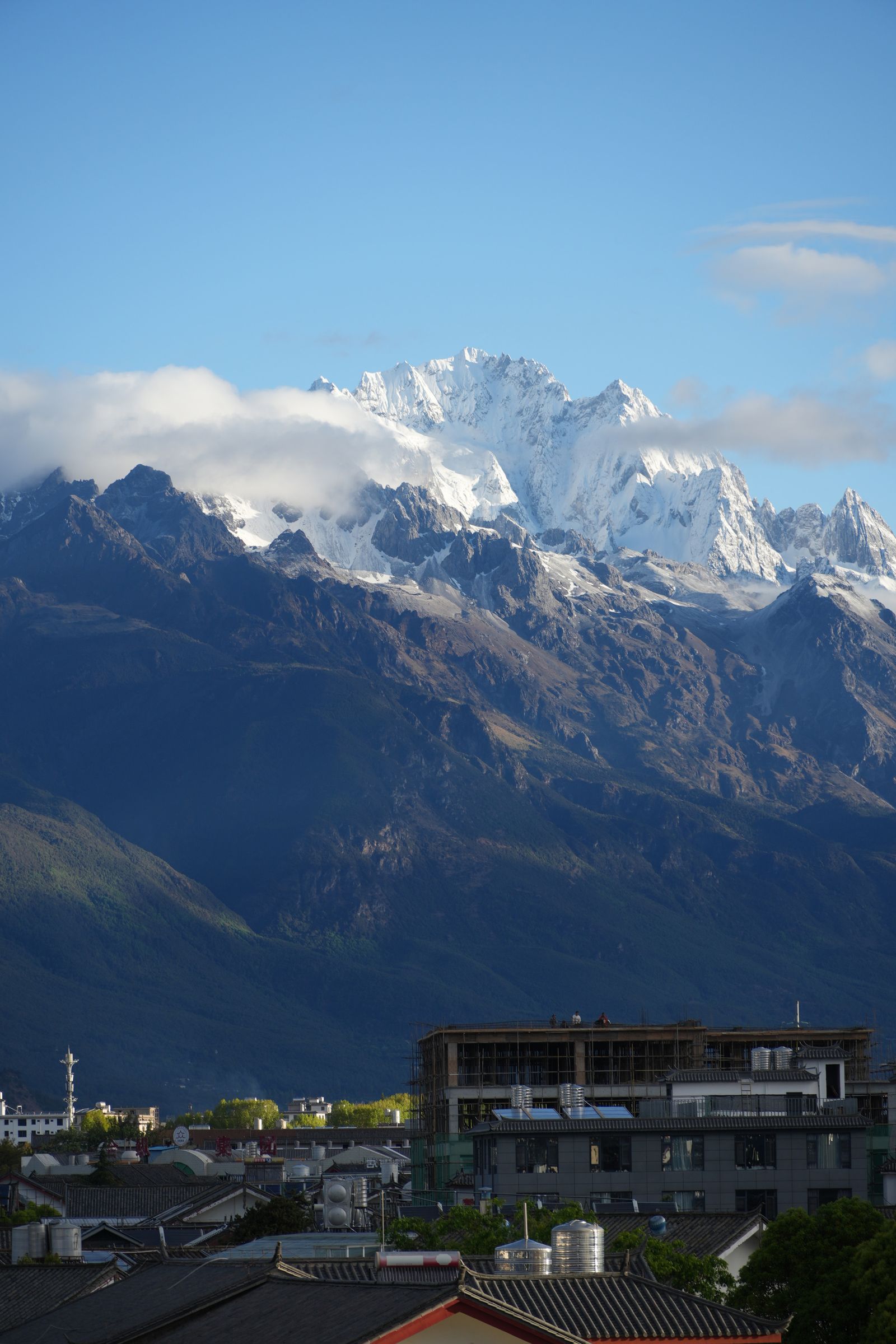 Snow-covered peaks above tiled rooftops and rooftop water tanks, Tiger Leaping Gorge