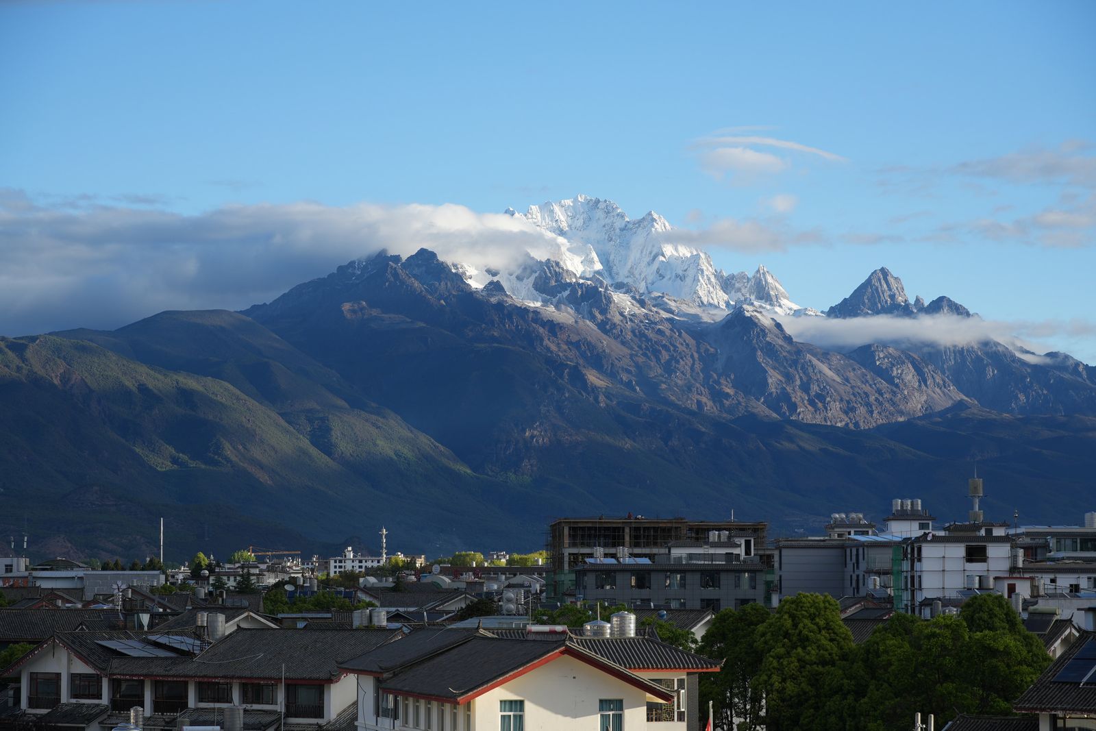 Snow-covered peaks above green slopes and white buildings, Tiger Leaping Gorge