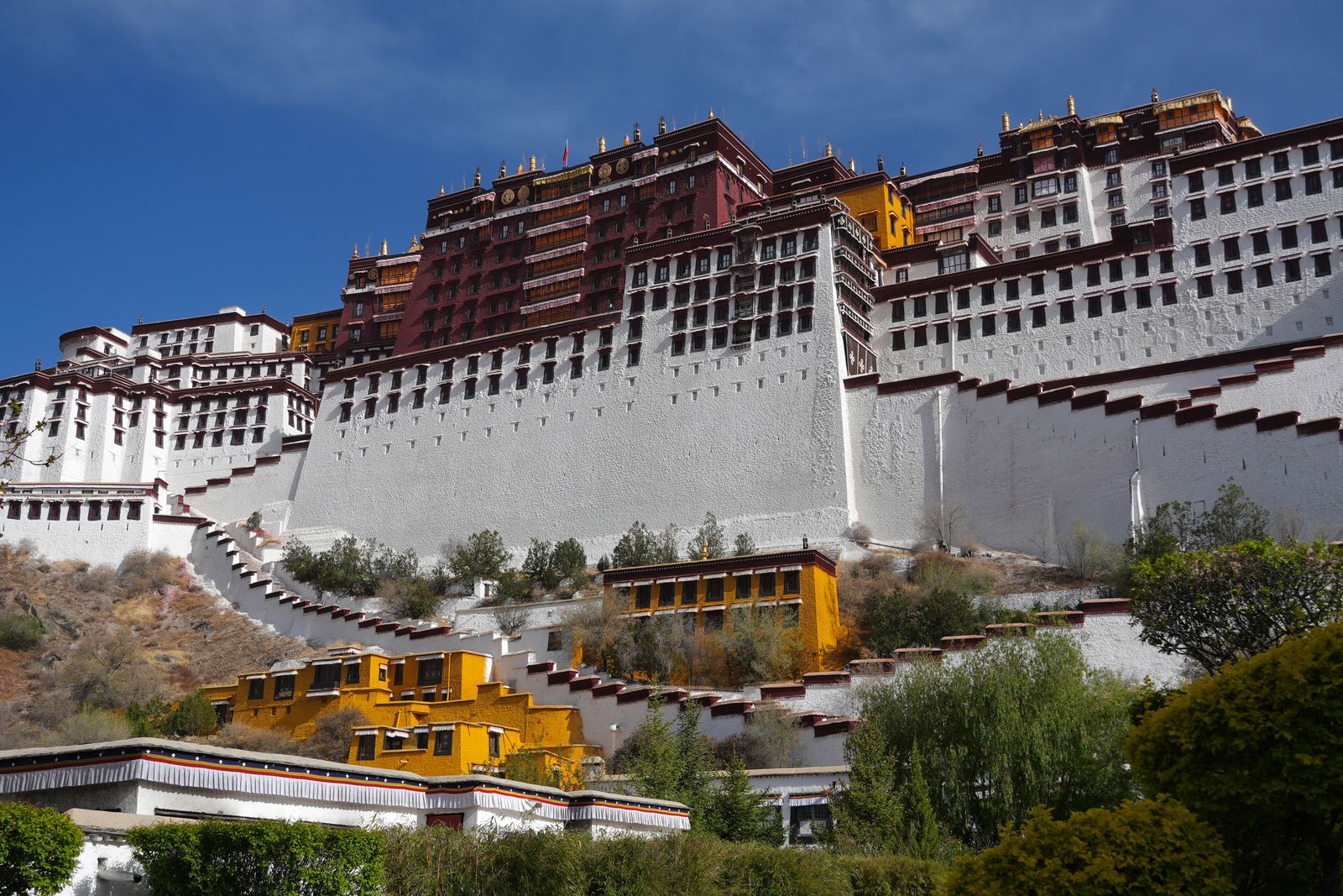 Temple complex above stepped white walls and trees, Tibetan plateau