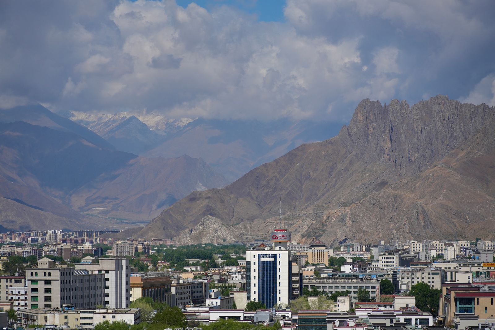 A rocky ridge above city buildings below snow-covered peaks, Tibetan plateau