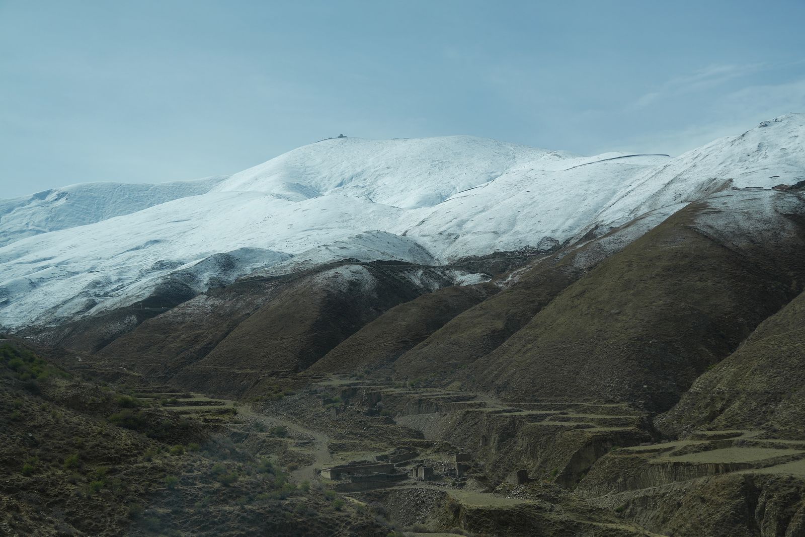 Snow-covered mountains above brown slopes and terraced ground, Tibetan plateau