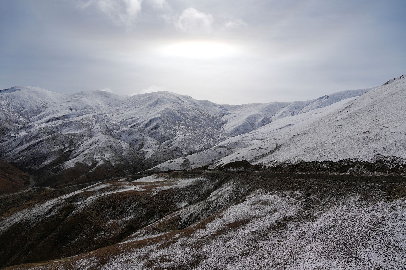 Snow-covered mountains above a winding road under gray clouds, Tibetan plateau