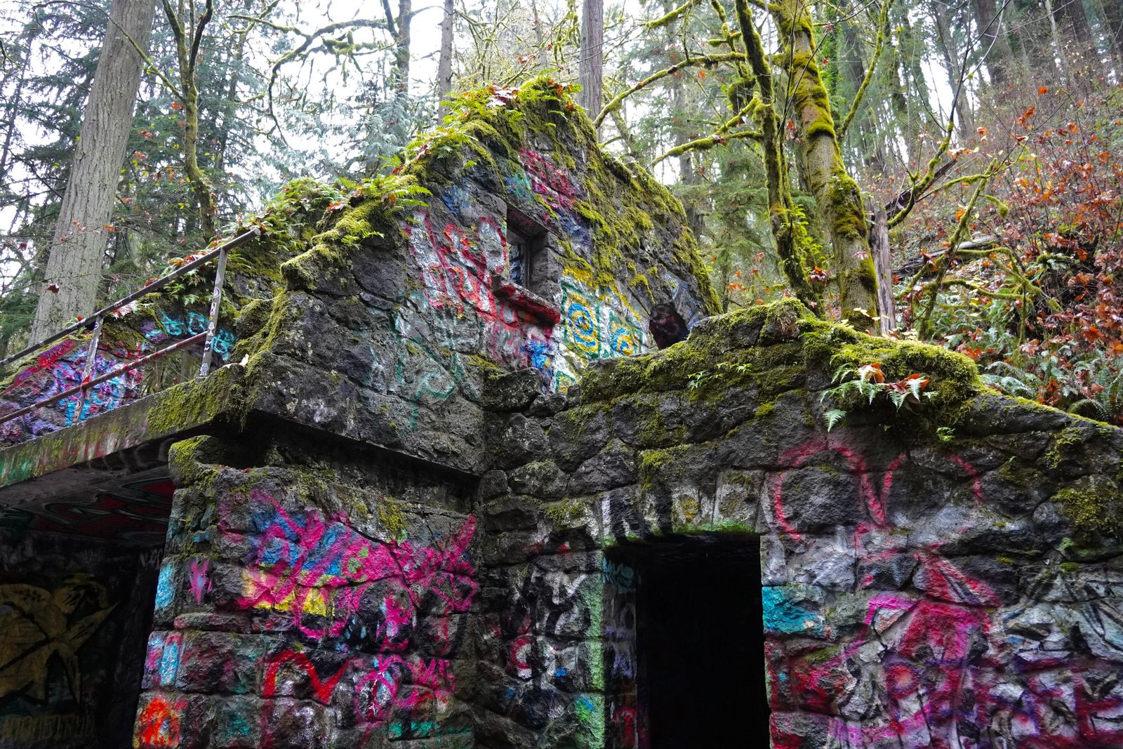 A graffiti-covered stone structure among moss-covered trees, Portland