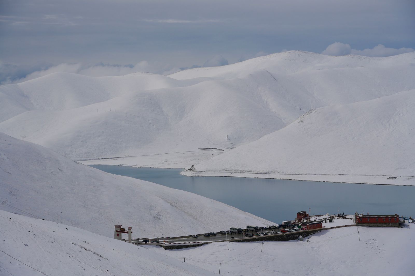 Red buildings beside a lake surrounded by snow-covered hills, Tibetan plateau