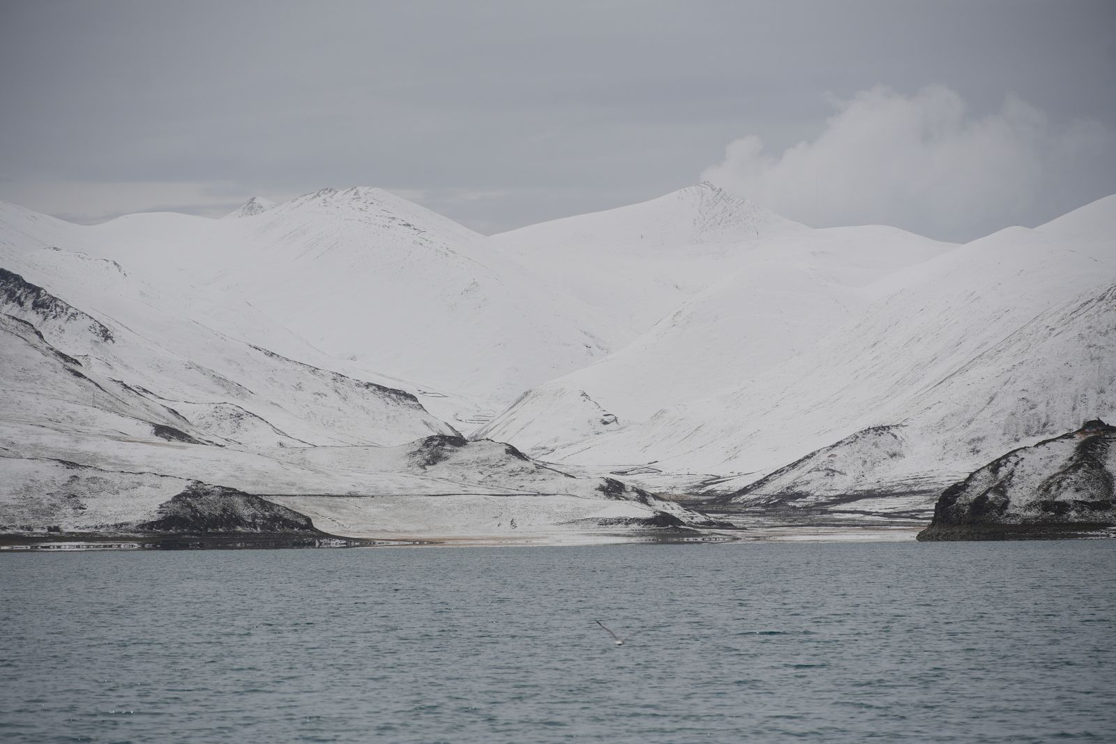 Snow-covered mountains above a lake with rocky shores, Tibetan plateau