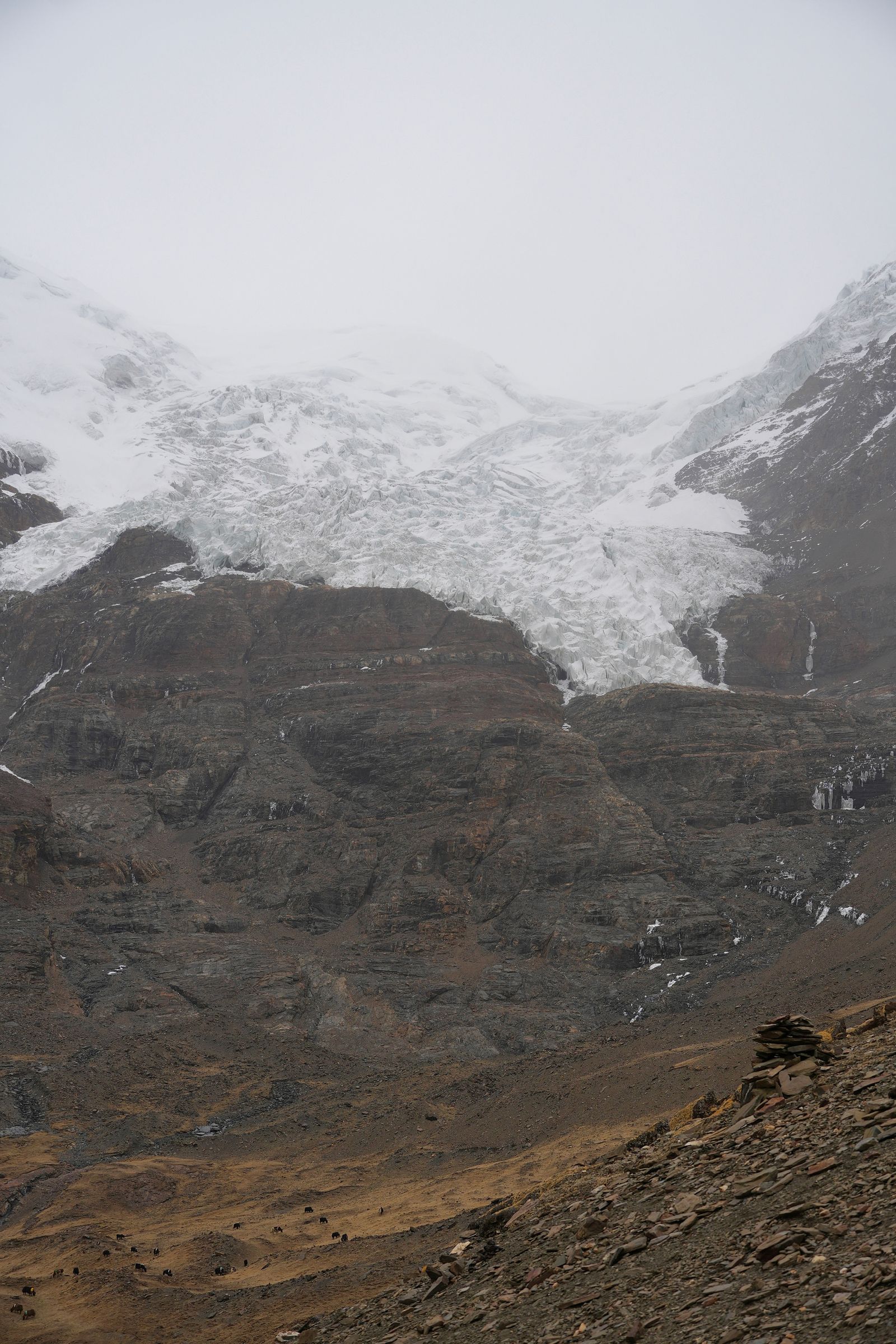 A glacier above rocky cliffs with a stone cairn, Tibetan plateau