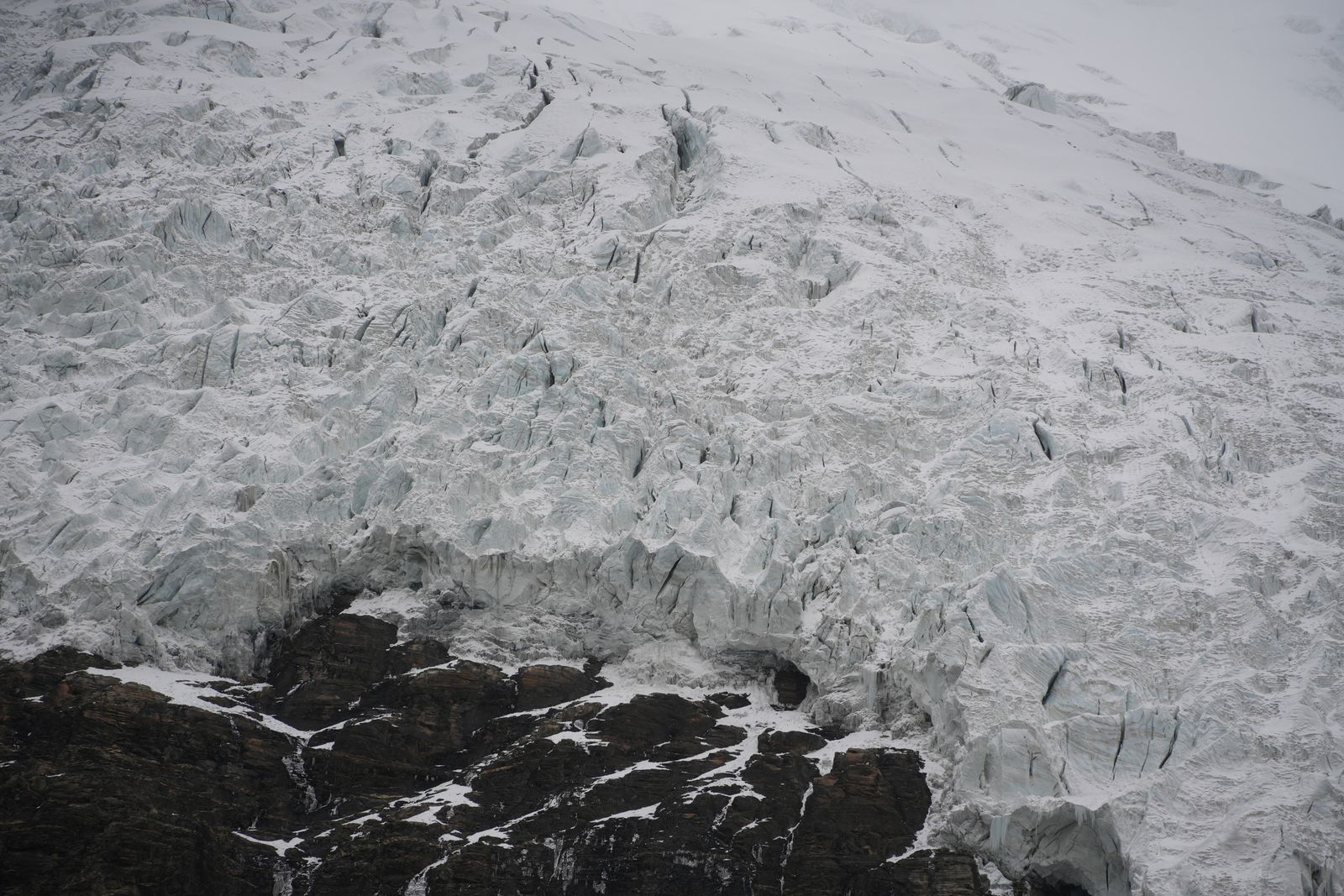 A cracked glacier above dark exposed rock, Tibetan plateau