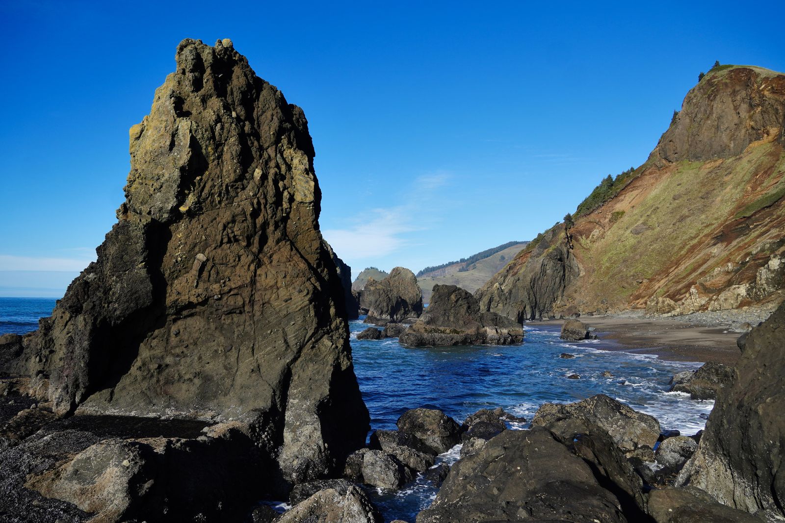 A sea stack beside surf and a grass-covered cliff, Gods Thumb