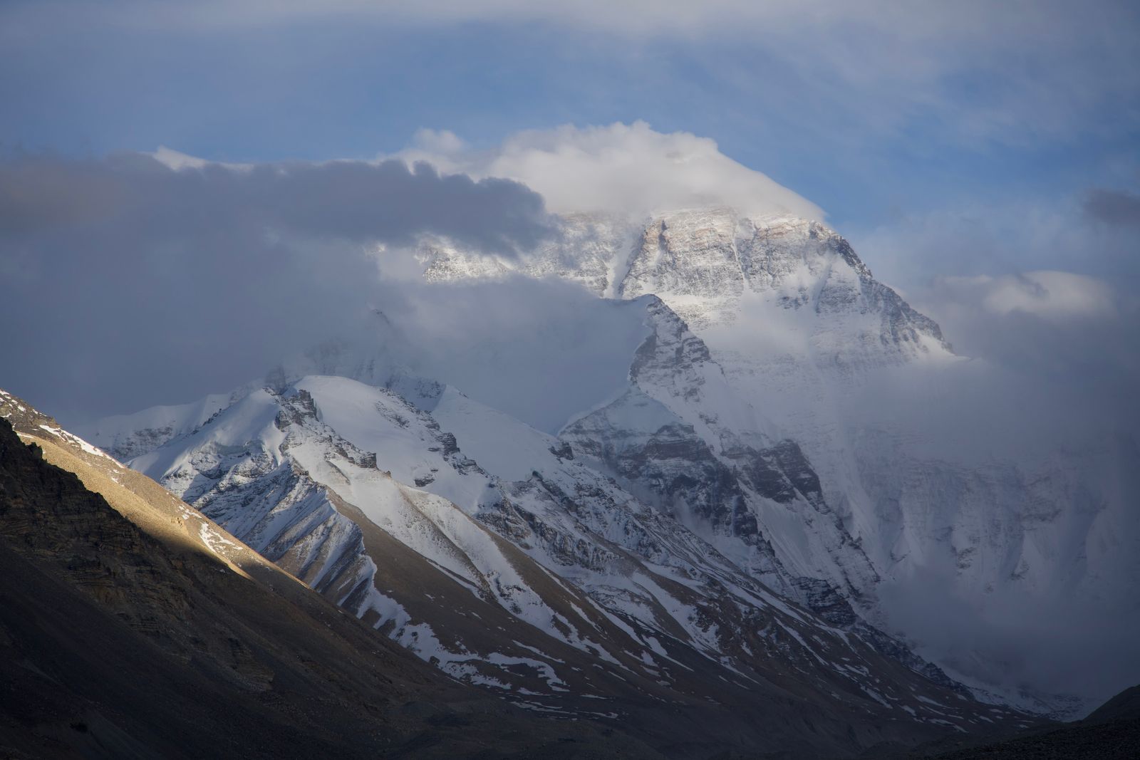Everest north face partly hidden by clouds above dark ridges