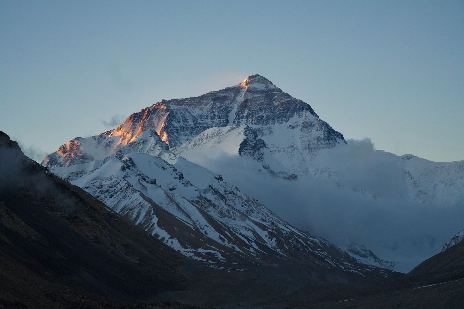 Mount Everest in warm light above dark rocky slopes
