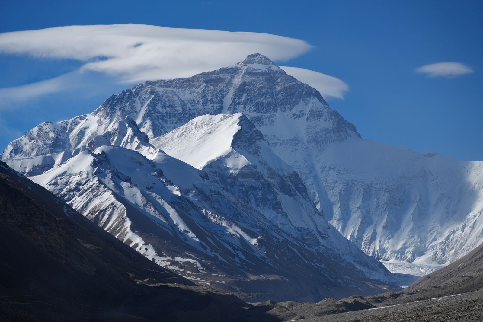 Mount Everest above rocky slopes beneath broad white clouds