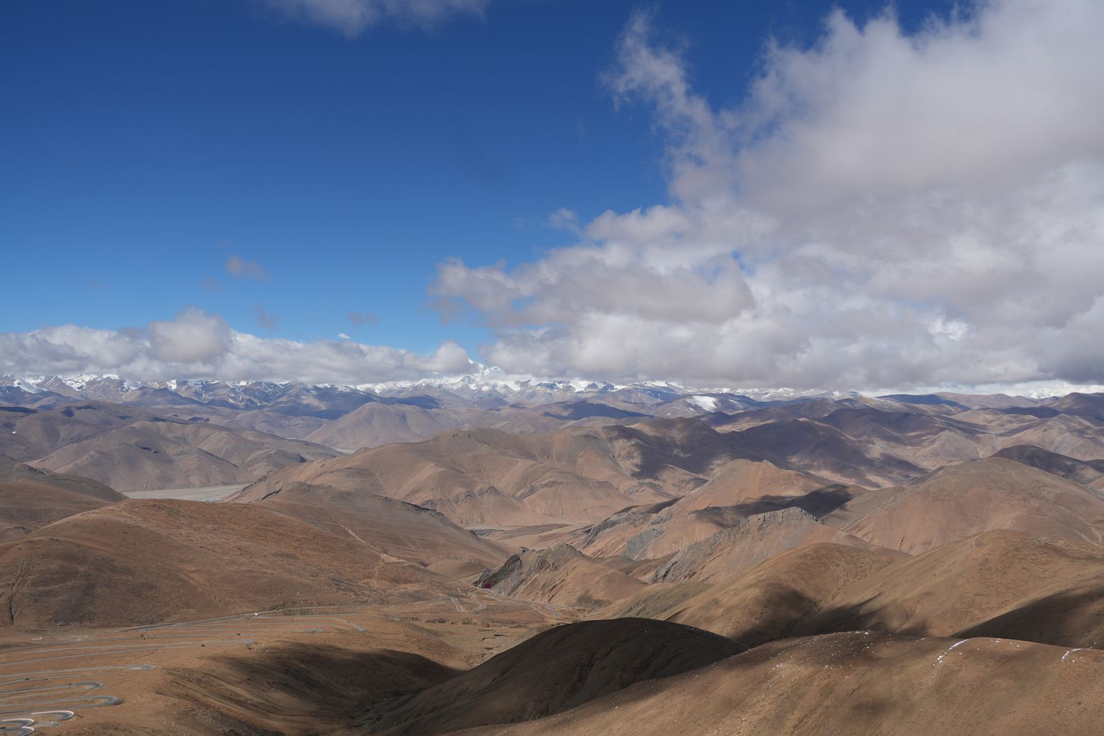A winding road through brown ridges below snow-covered peaks, Tibetan plateau