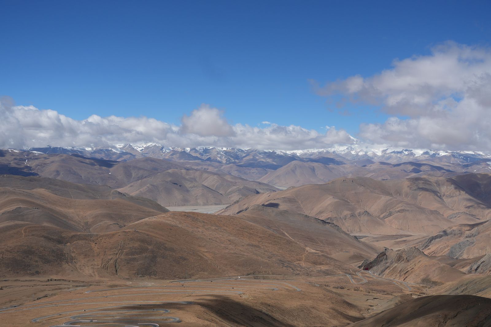 A winding road through brown ridges below snow-covered peaks, Tibetan plateau