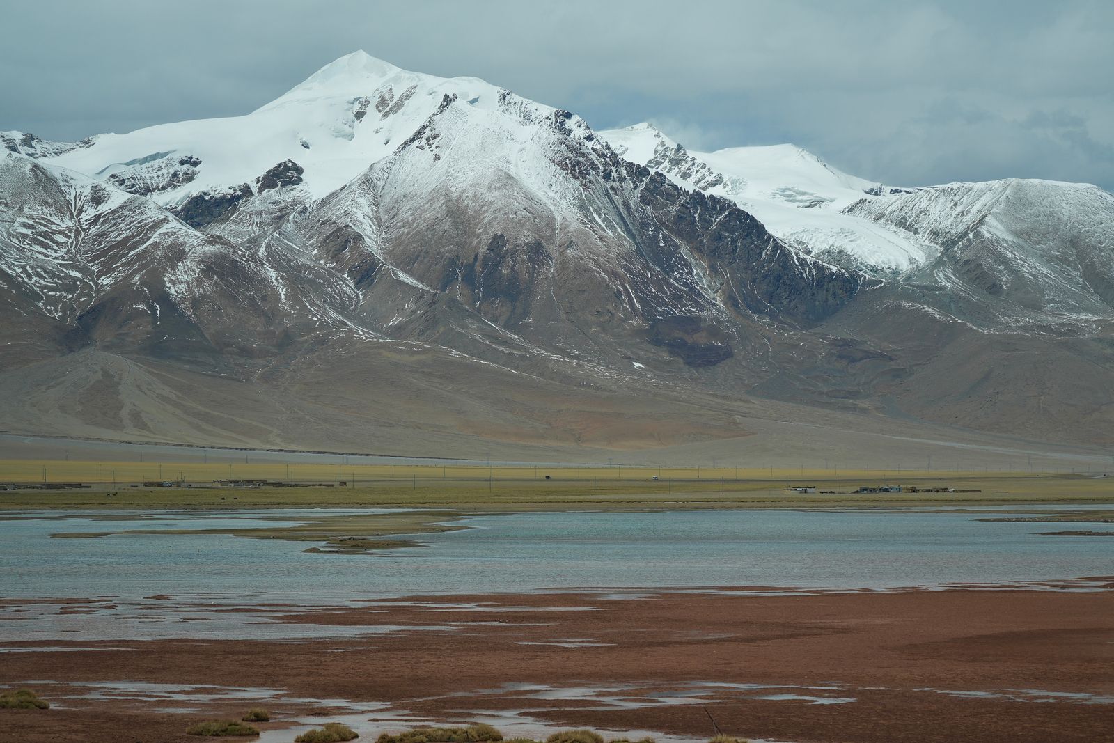 Snow-covered peaks above water and reddish flats, Tibetan plateau