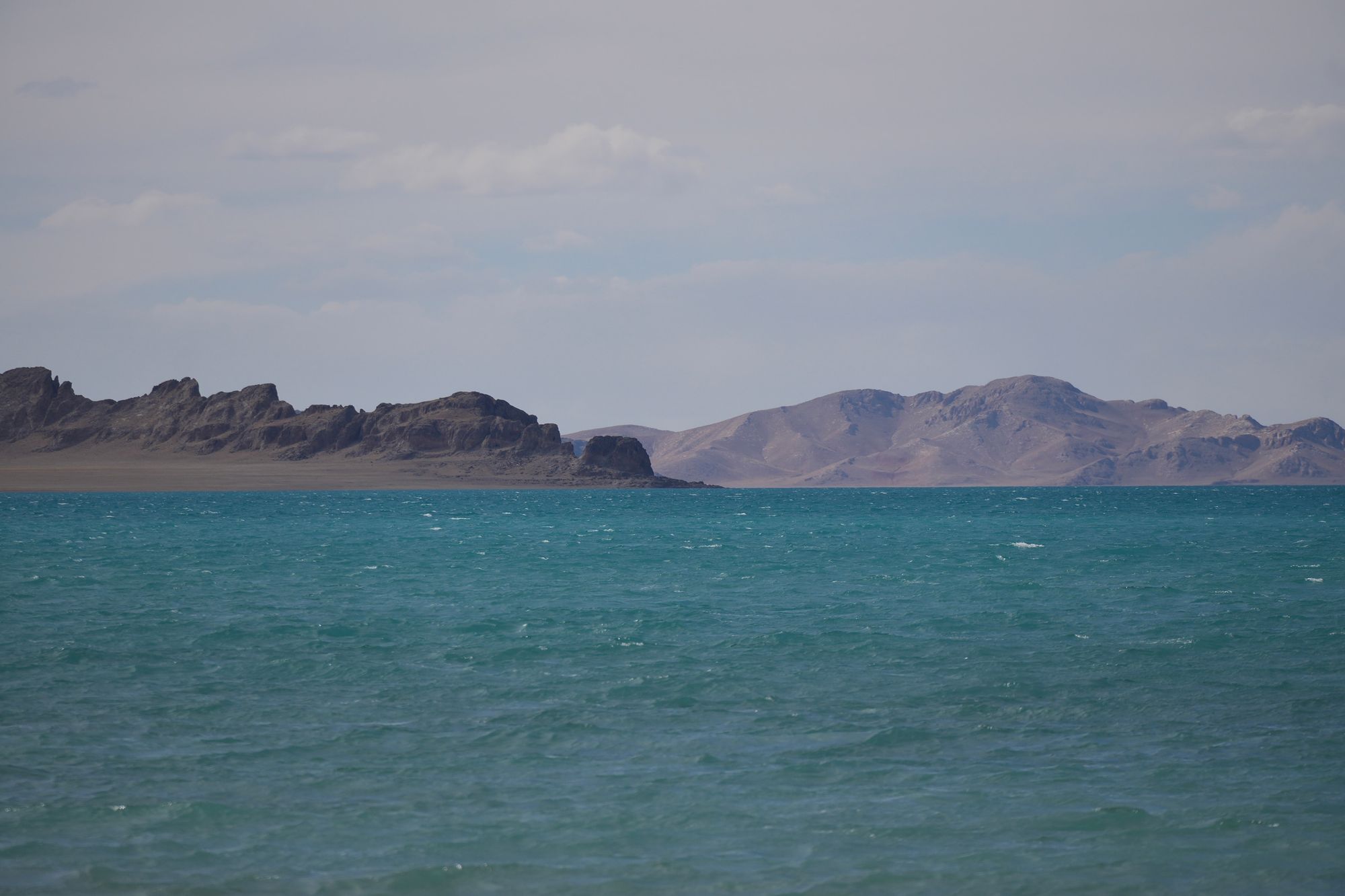 Turquoise lake with whitecaps below bare rocky ridges, Tibetan plateau