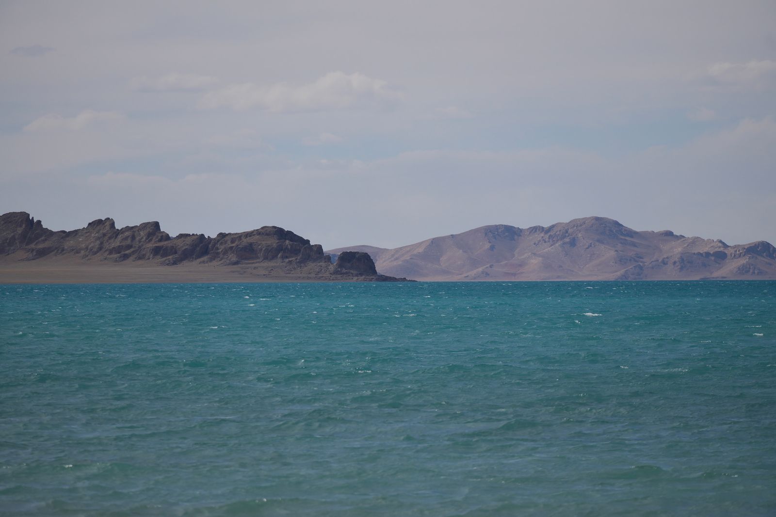 Turquoise lake with whitecaps below bare rocky ridges, Tibetan plateau