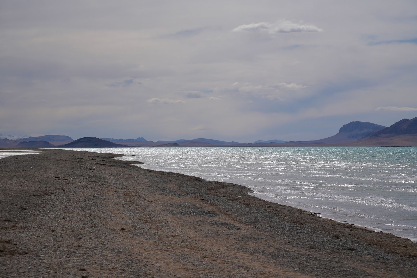 A turquoise lake beside a gravel shore and bare mountains, Tibetan plateau
