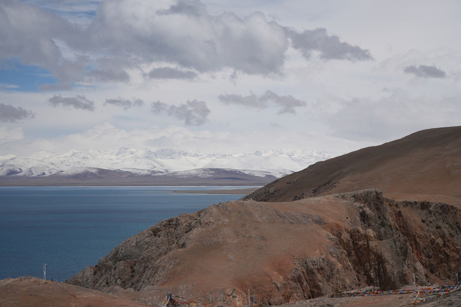 A blue lake with colored flags below snow-covered mountains, Tibetan plateau