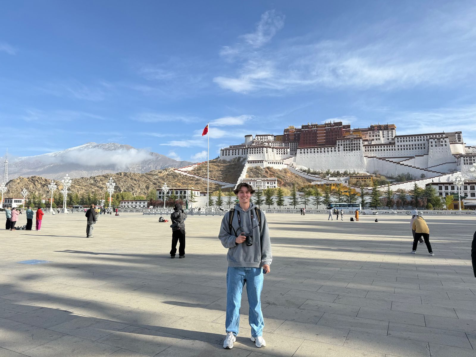 A person holding a camera below a hillside building, Tibetan plateau