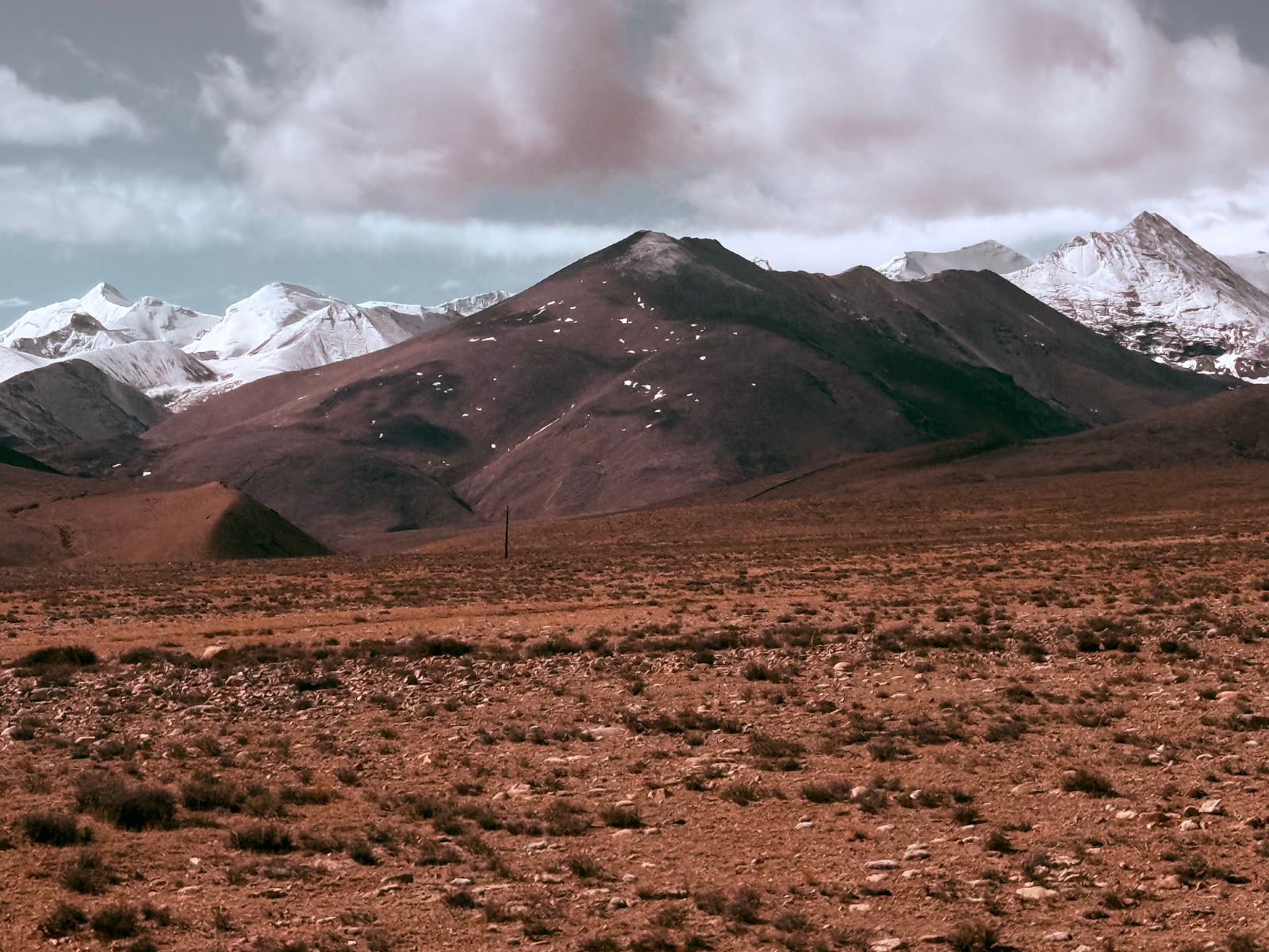 Snow-covered peaks beyond dark mountain ridges under grey clouds, Everest north face