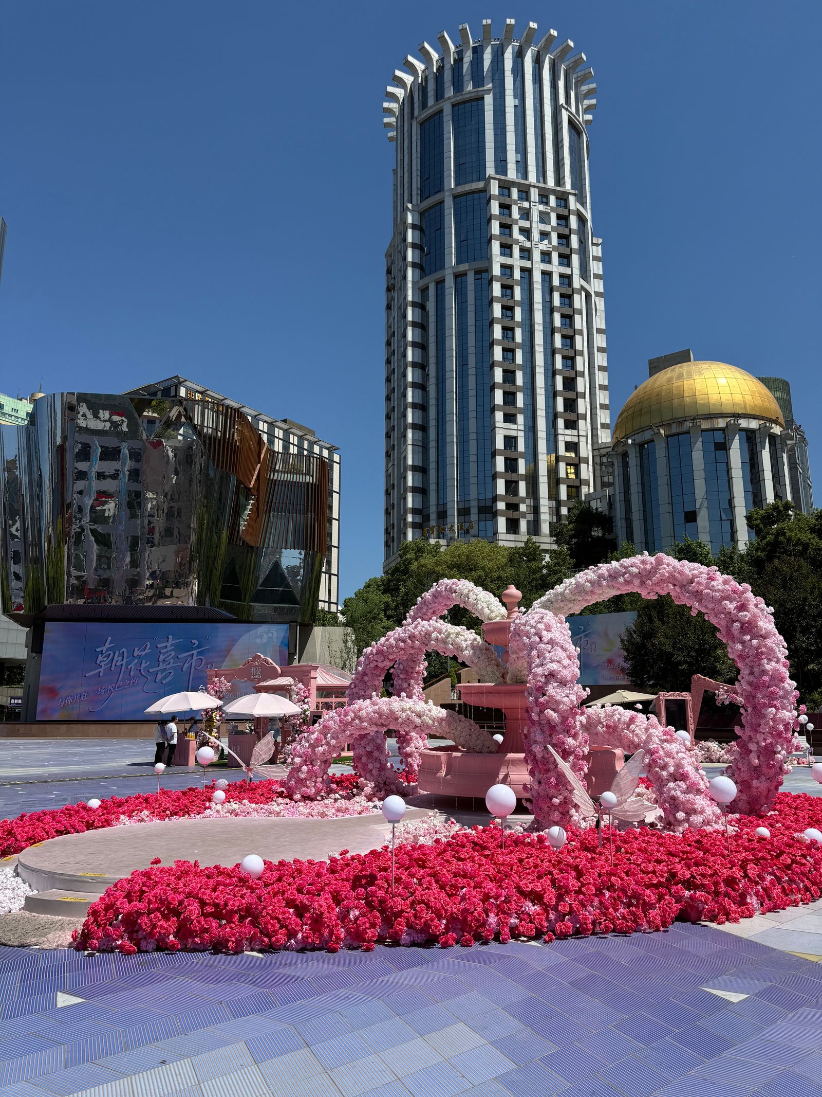 Pink floral arches around a fountain below tall buildings, Shanghai