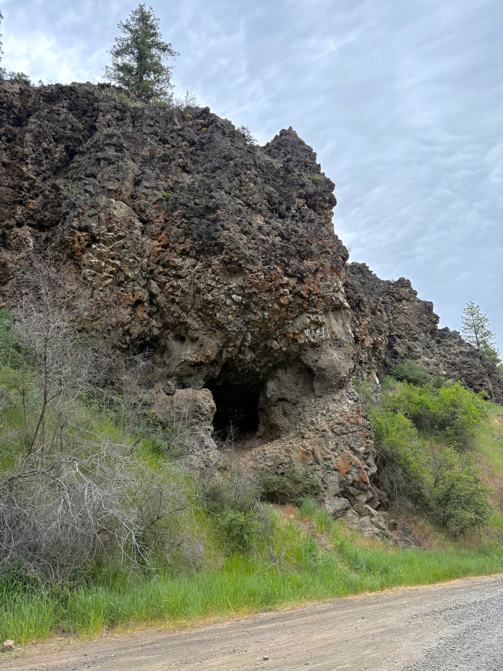 Rock outcrop with a dark opening above a gravel road, shrub-steppe