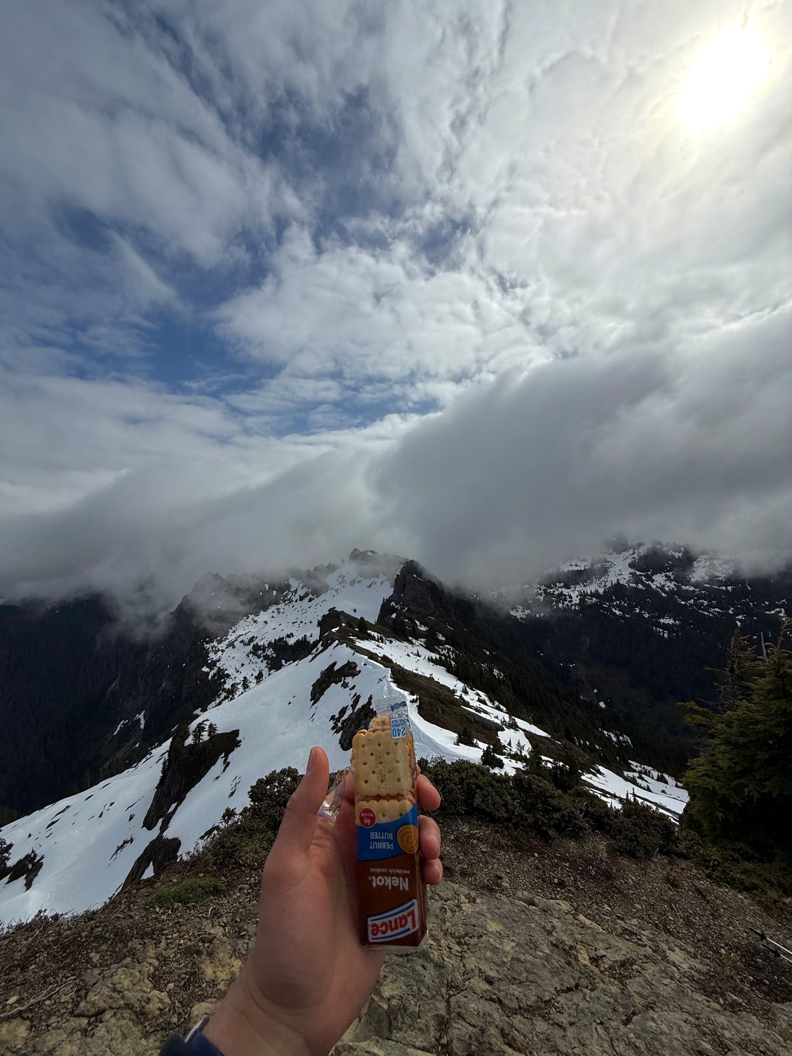 Packaged crackers held before snowy ridges under low clouds, Ball Mountain