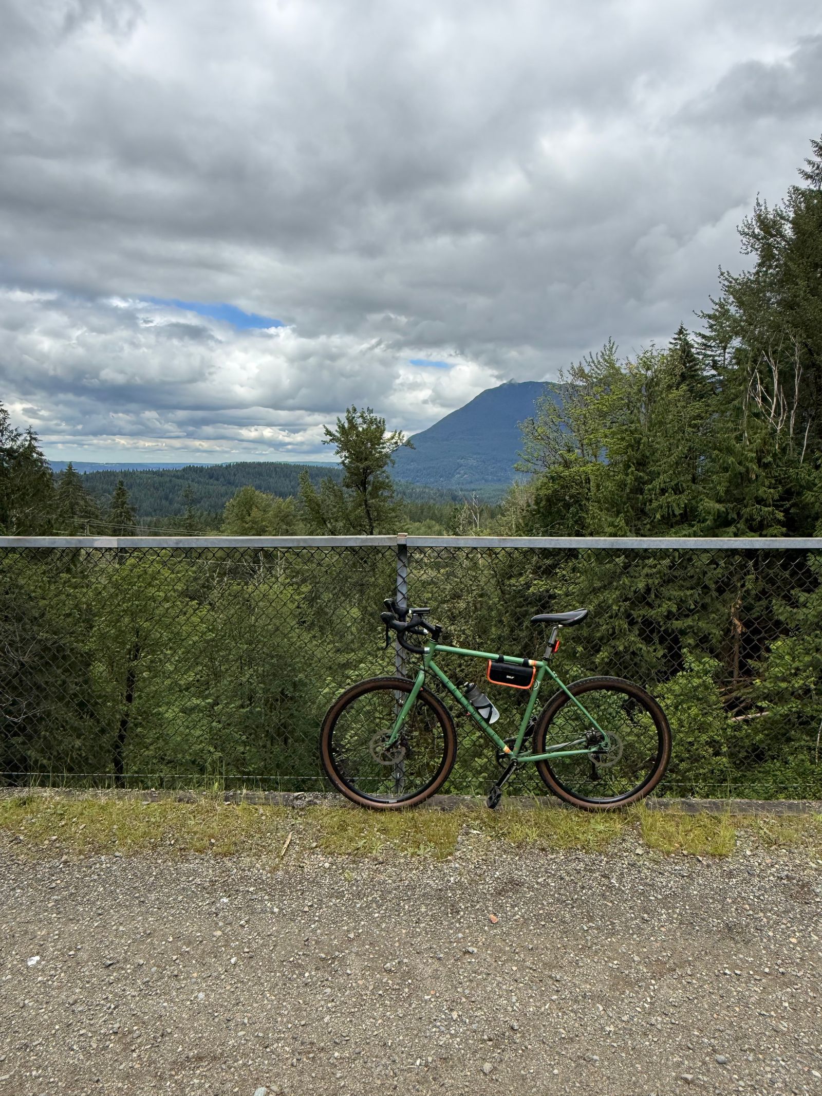 A green bicycle beside a fence below a forested mountain, Gunn Peak