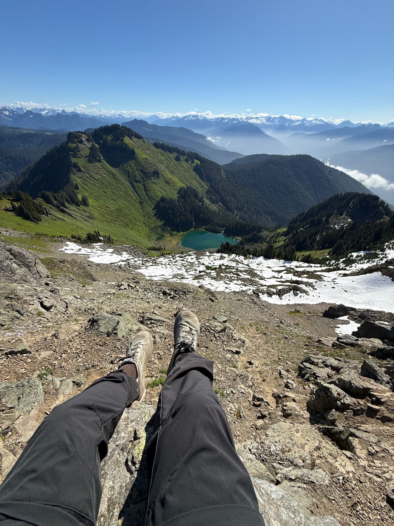 A person's legs above a tarn and snowy ridges, Sauk Mountain