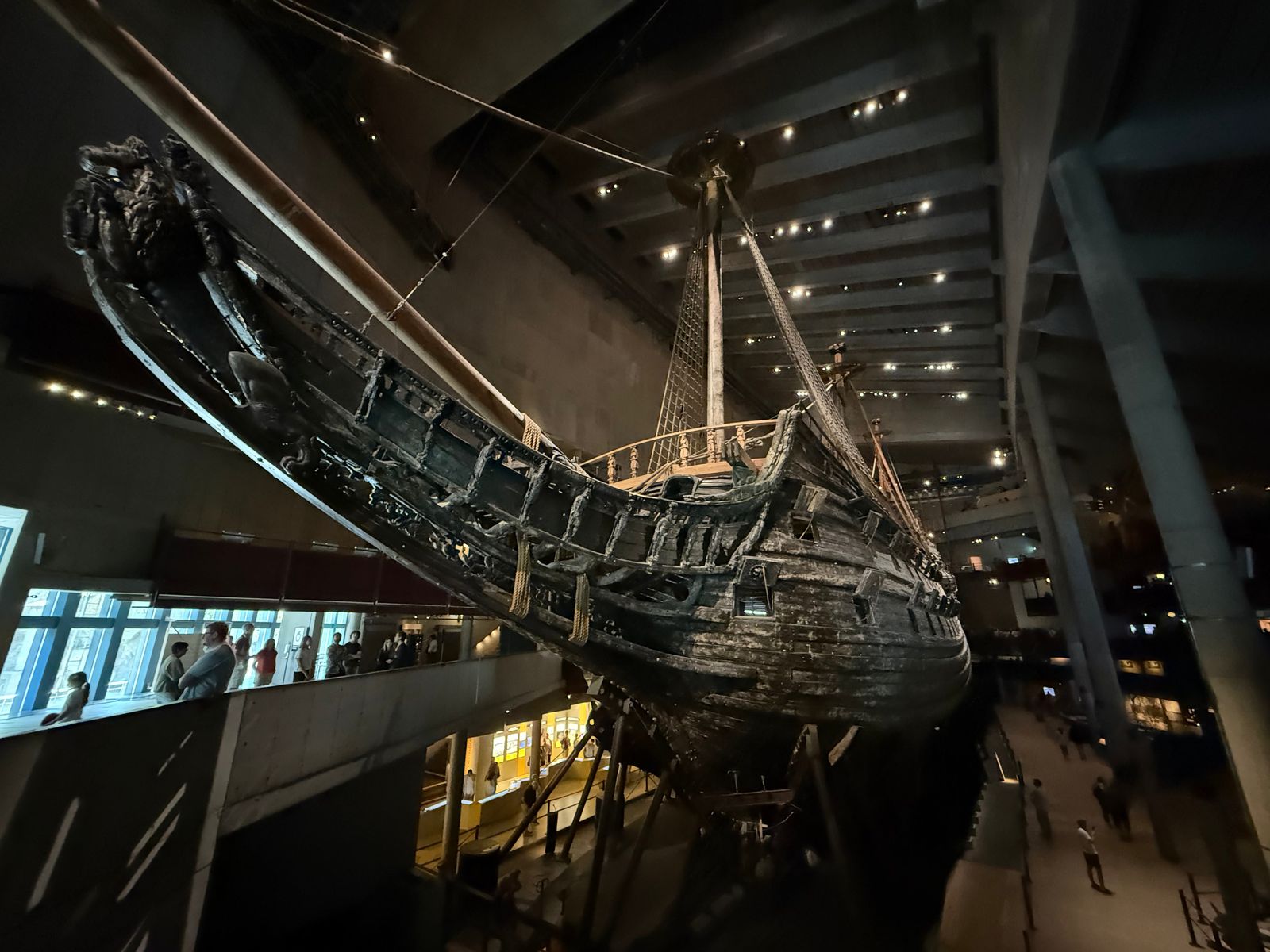 Wooden ship with exposed hull timbers above visitors under spotlights, Stockholm