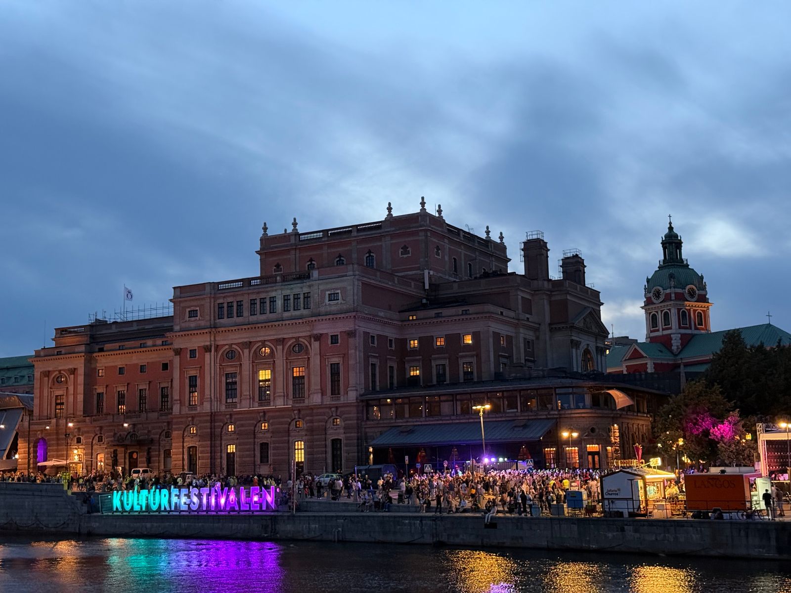 Waterfront buildings and lit signs reflected in dark water, Stockholm
