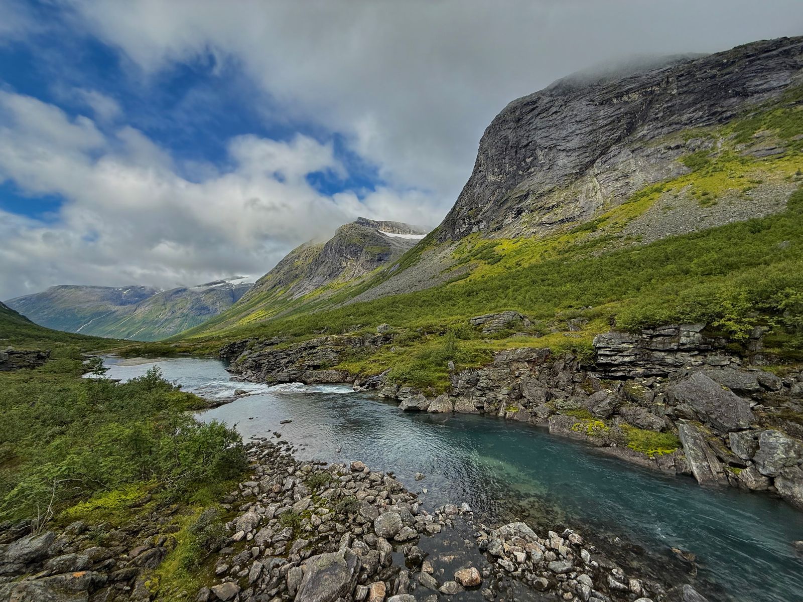 River between rocky banks below mountains under low clouds, Trollstigen