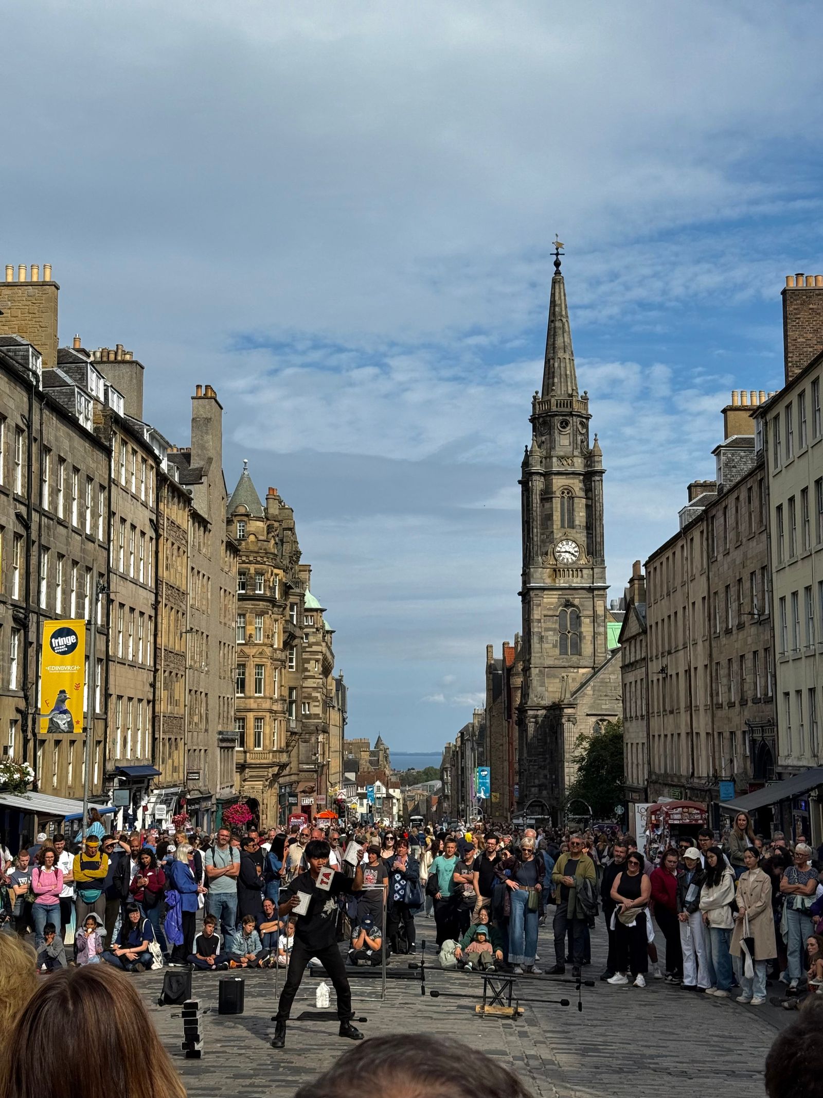 Street performer before a crowd below a stone clock tower, Edinburgh Town