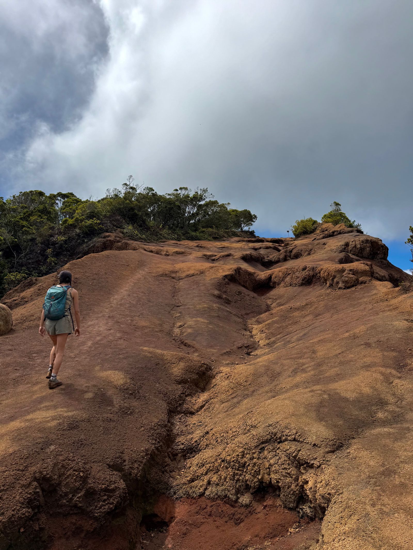 A hiker climbing an eroded slope under thick clouds, Napali Coast