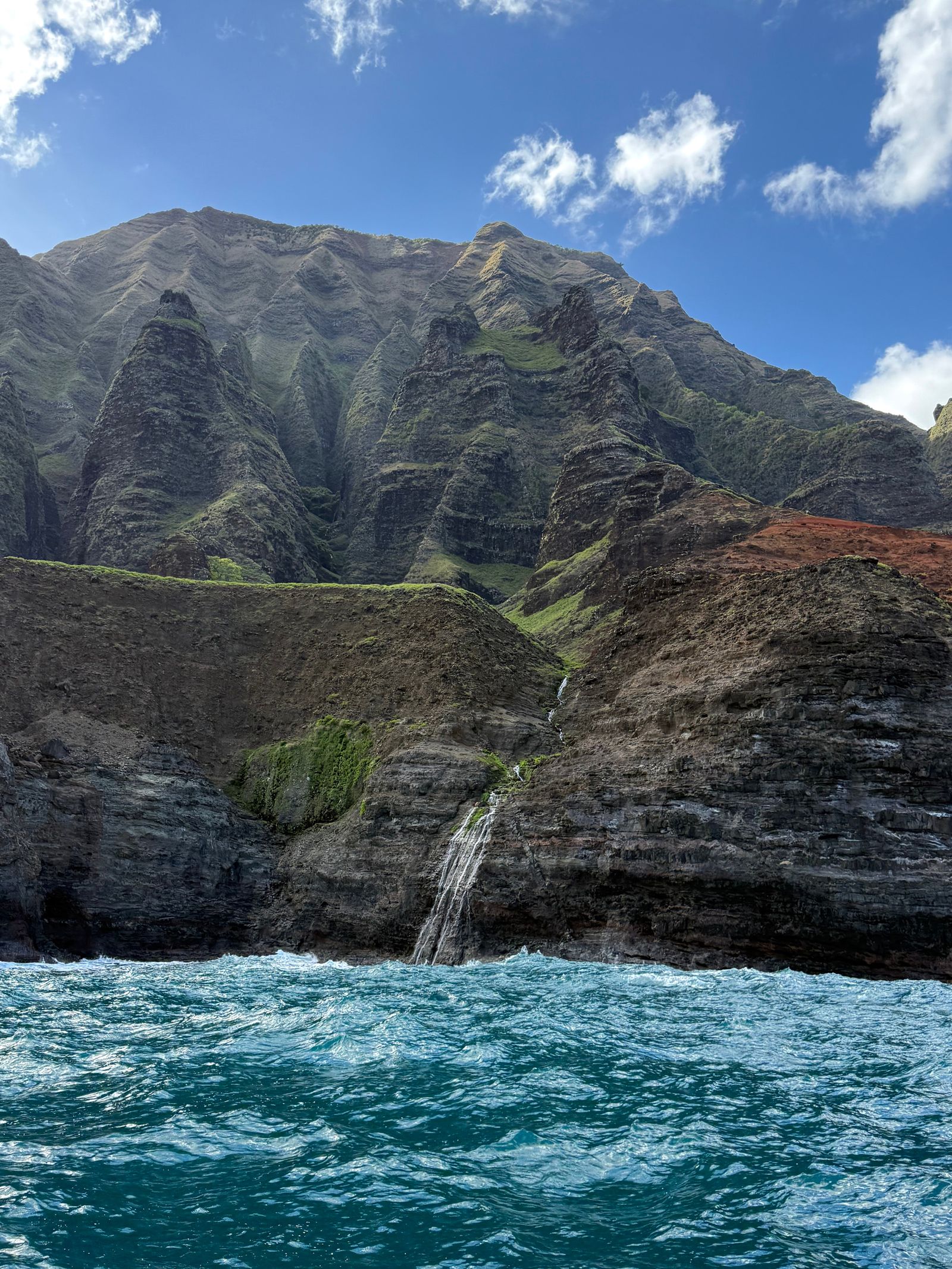 Napali Coast waterfall dropping down cliffs above choppy ocean water