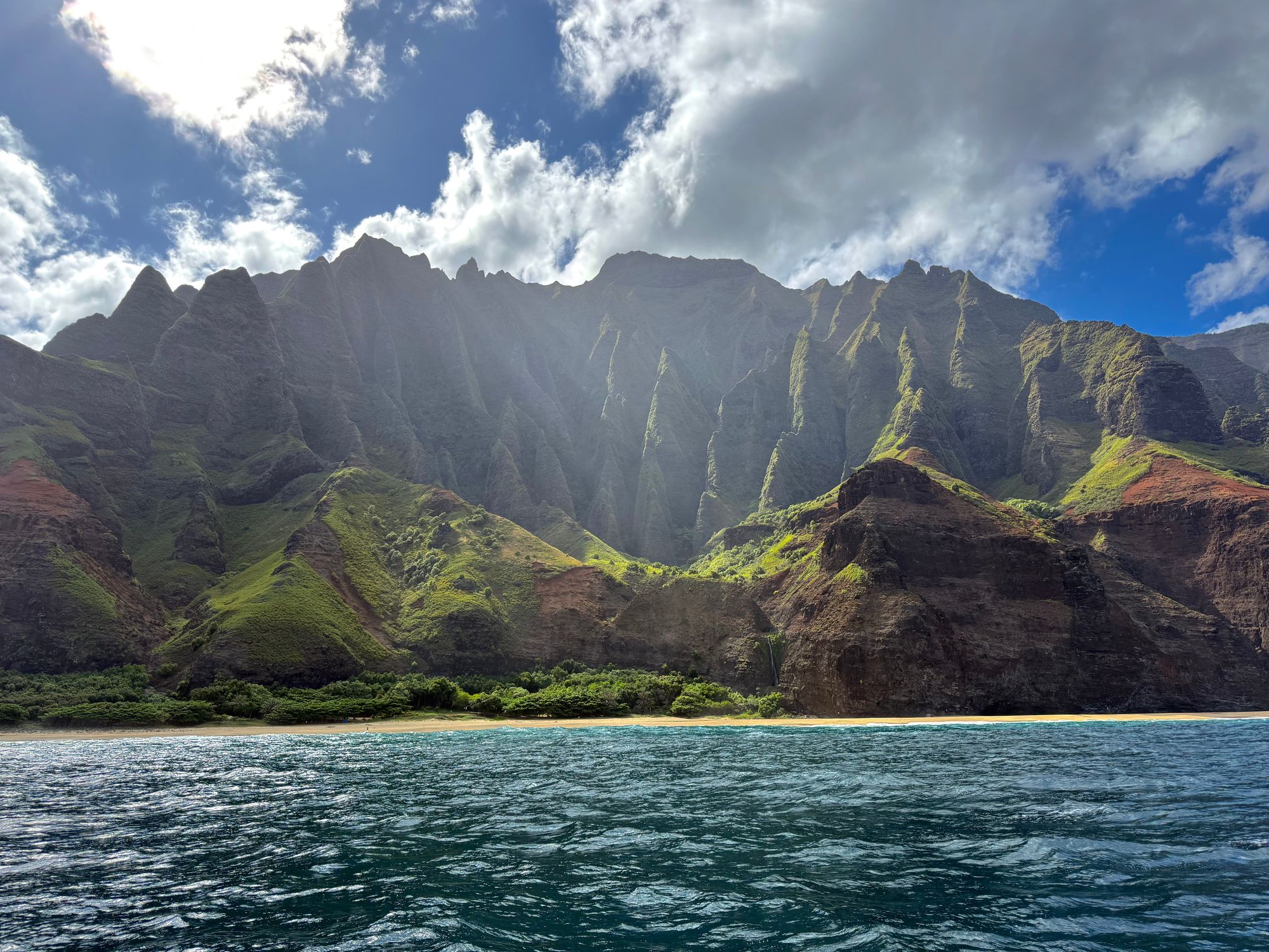 Backlit Napali Coast cliffs above a beach and rippled ocean