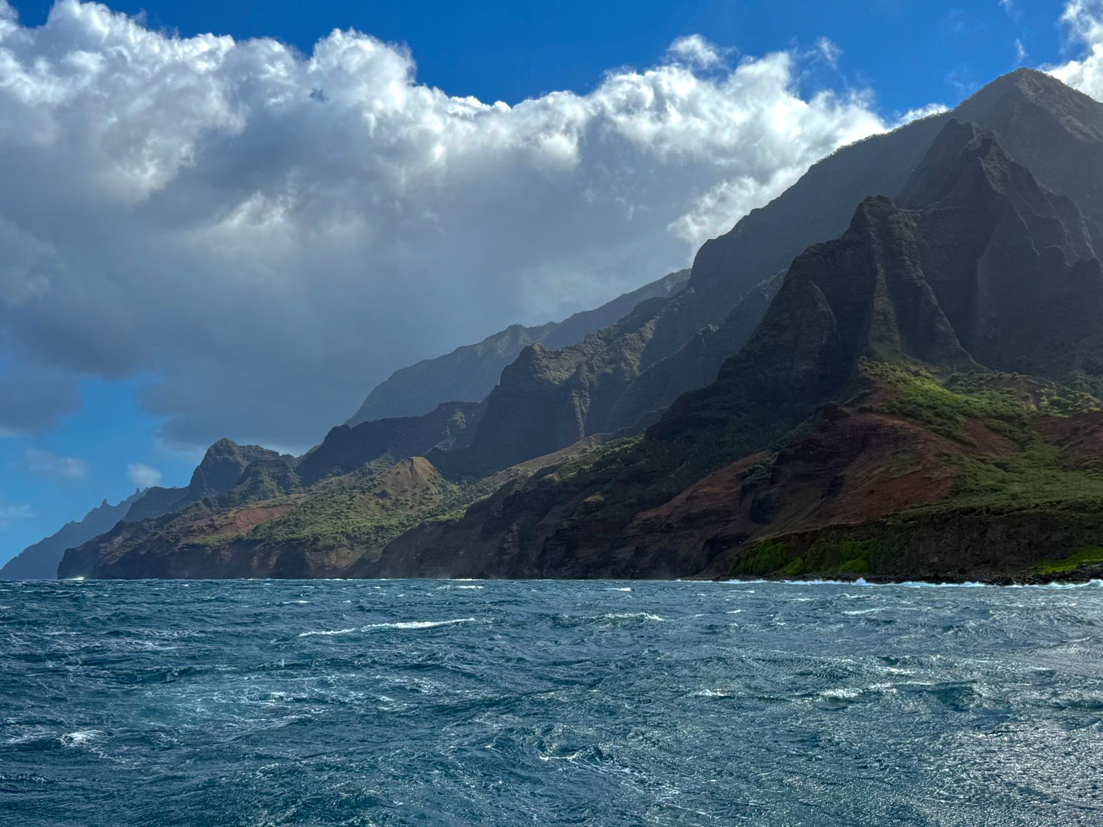 Napali Coast ridges above choppy ocean water under large clouds